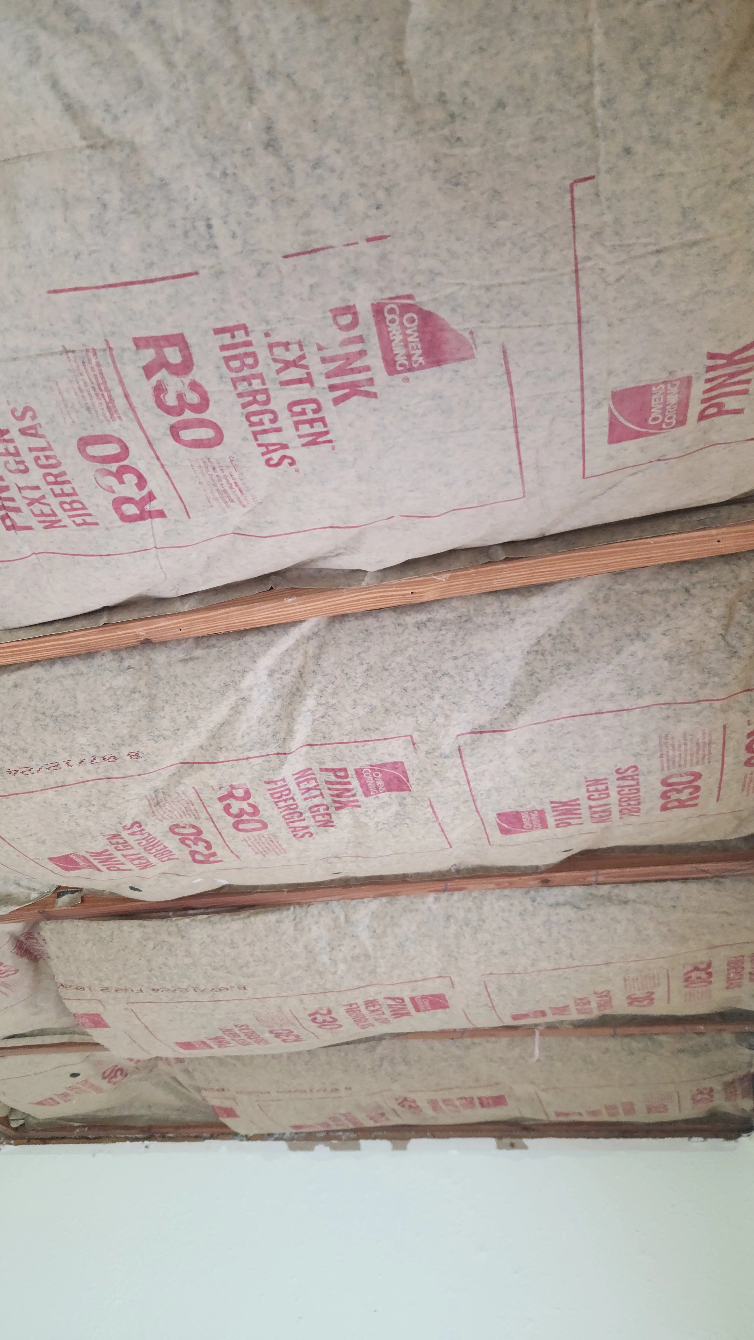 Bundles of fiberglass insulation wrapped in paper with pink text and logos, stacked on a wooden surface.