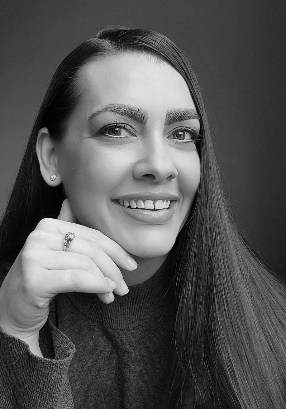 Black and white portrait of a woman with long hair, smiling, wearing earrings and a ring, looking at the camera.