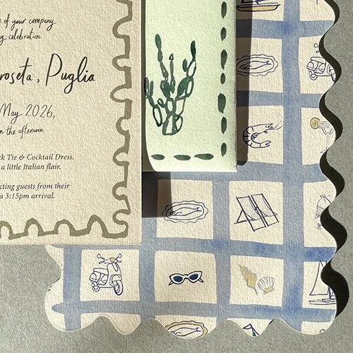 Close-up of a wedding invitation with decorative edges, featuring blue and beige checkered background with illustrations of seashells, starfish, sunglasses, and a scooter.
