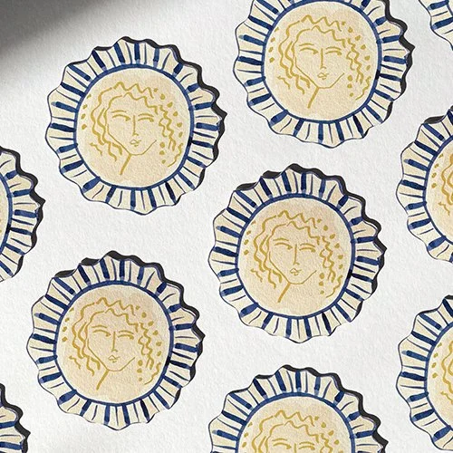 Pattern of circular designs featuring a woman's face in gold with curly hair, surrounded by a blue striped border, on a white background.