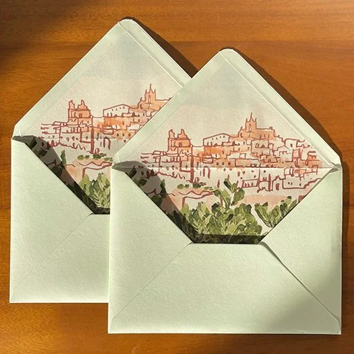 Two open envelopes with illustrated cityscape inside, placed on a wooden surface.