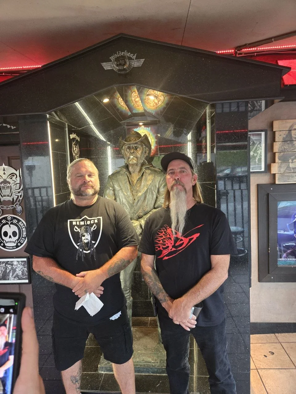 Two men standing in front of a bronze cowboy statue inside a restaurant, with decorative and framed artworks on the walls.