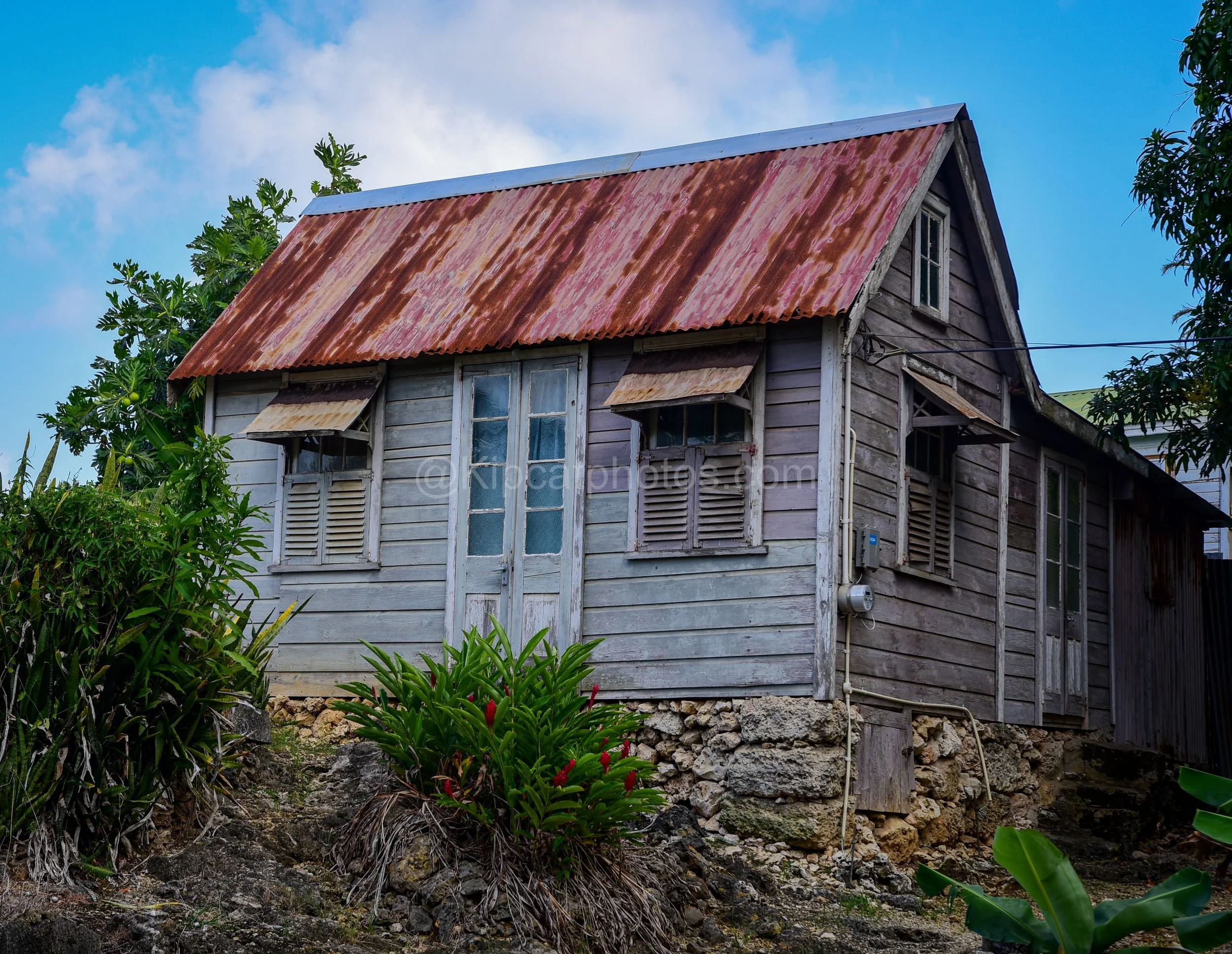 A grey wooden chattel house in Barbados with a rusted gable roof, jalousie windows and a coral stone foundation. Kipcatphotos.com

Faded grey clapboard walls and rust-streaked corrugated roofing give this Barbadian chattel house real character, with 