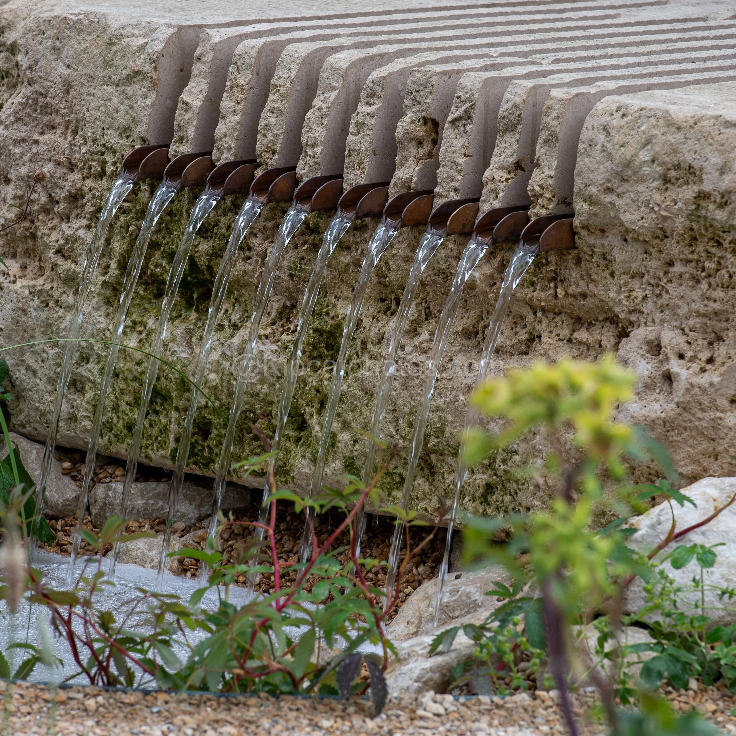 Row of copper spouts feeding water down a textured stone rill in the Joe & Laura Carey garden at RHS Chelsea Flower Show 2026

A row of small copper spouts channels water in delicate streams down a moss-covered stone rill, in the Joe & Laura Carey ga