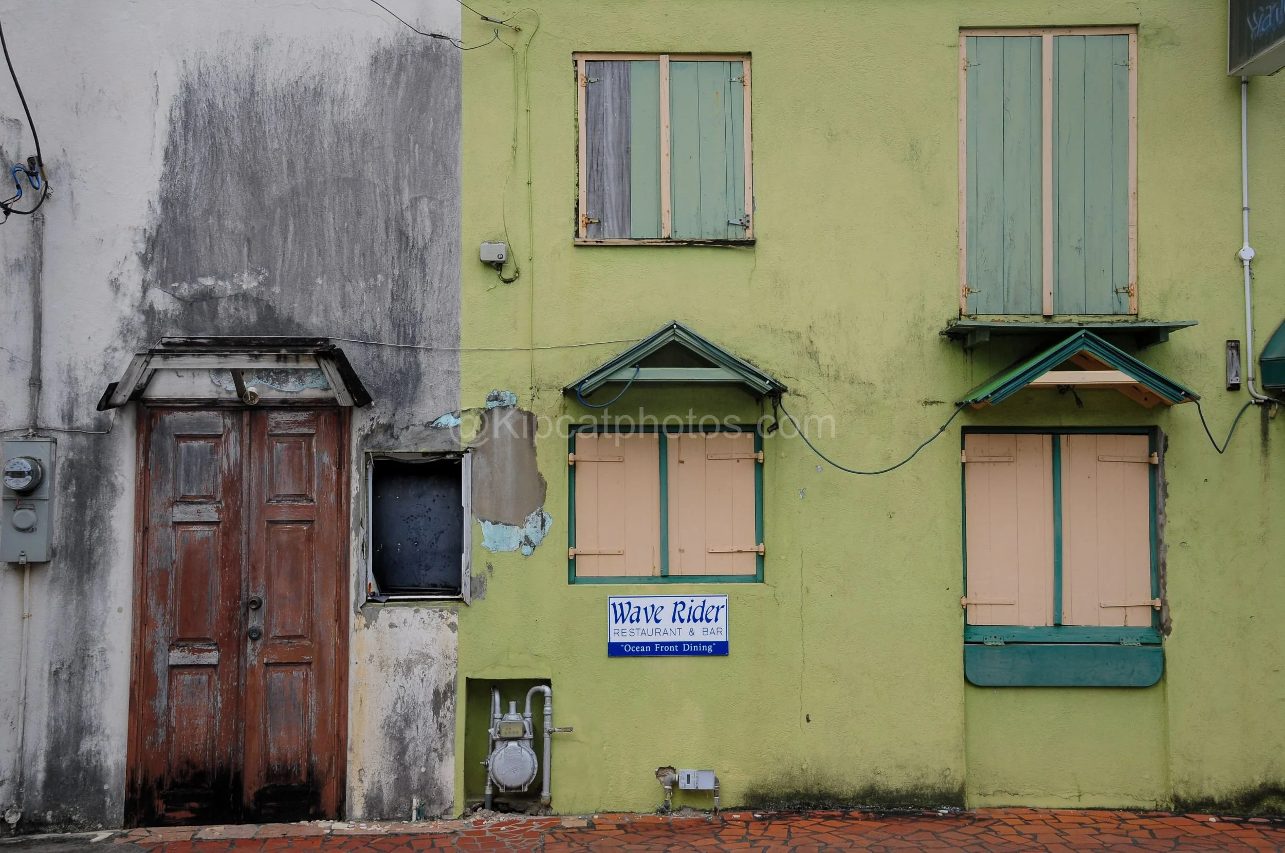 A green and white building facade in Barbados with shuttered windows and a Wave Rider Restaurant & Bar sign. Kipcatphotos.com

A weathered wooden door and pastel-shuttered windows front this lime green and white building, its faded blue "Wave Rider R