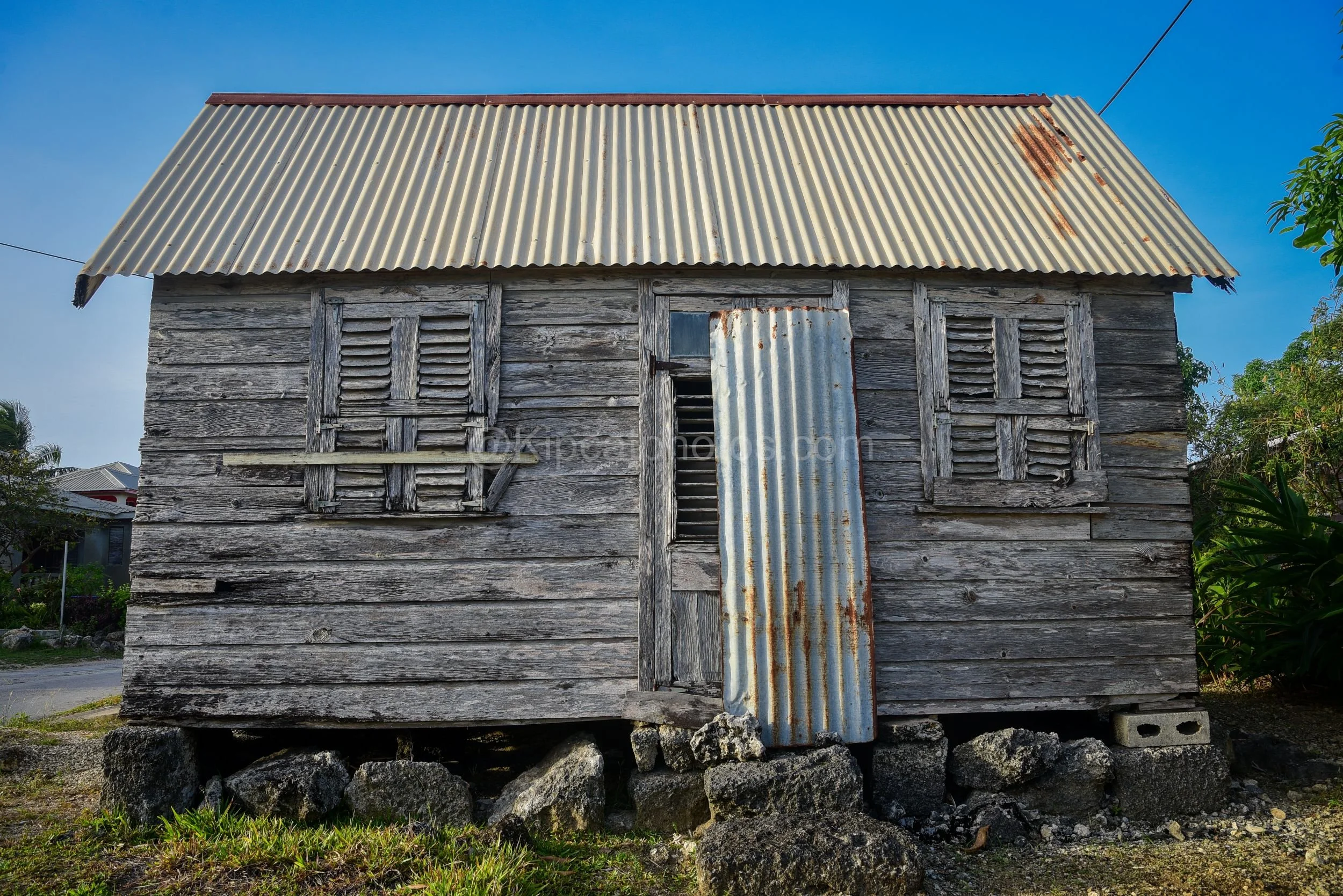 A grey wooden chattel house in Barbados with louvred shutters and a patched corrugated tin door. Kipcatphotos.com

Silvered by age, this chattel house's timber walls and louvred window shutters show the classic Barbadian vernacular style, with a corr