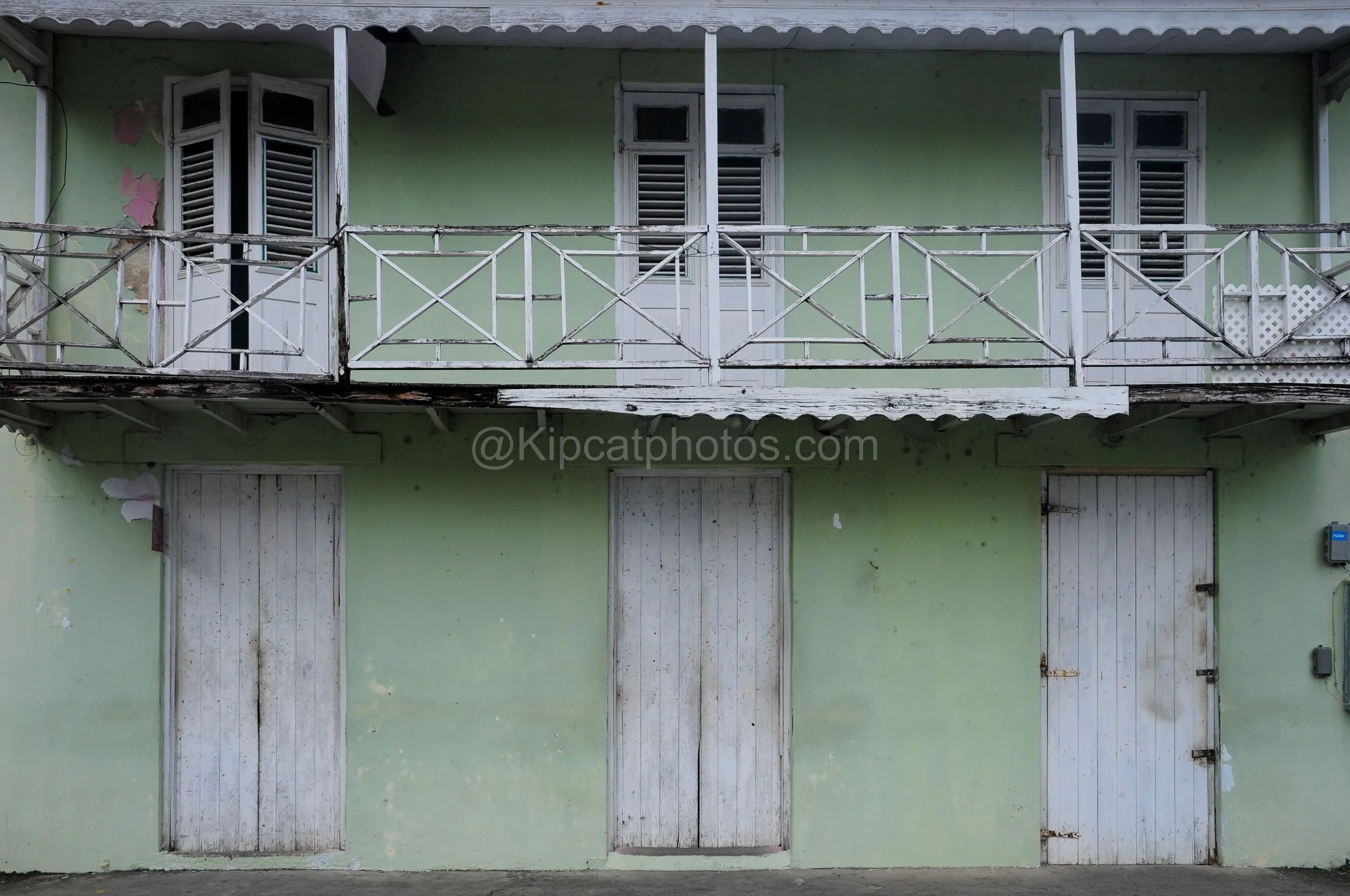 A weathered mint green two-storey building in Barbados with a crisscross balcony railing and louvred shutters. Kipcatphotos.com

Pale mint green paint covers this two-storey building's walls, its upper balcony enclosed by a white crisscross railing a
