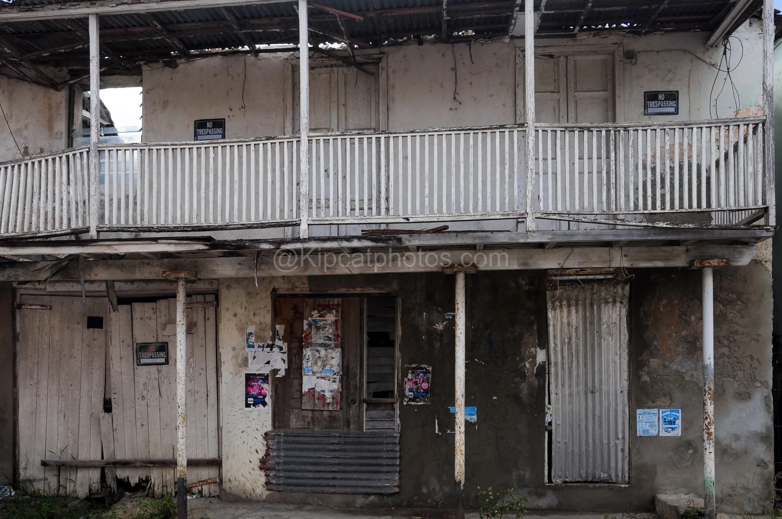 A derelict two-storey building in Barbados with a collapsing balcony and "No Trespassing" signs. Kipcatphotos.com

Peeling white balustrades and a partly caved-in corrugated roof mark this abandoned two-storey building, its ground floor doors plaster