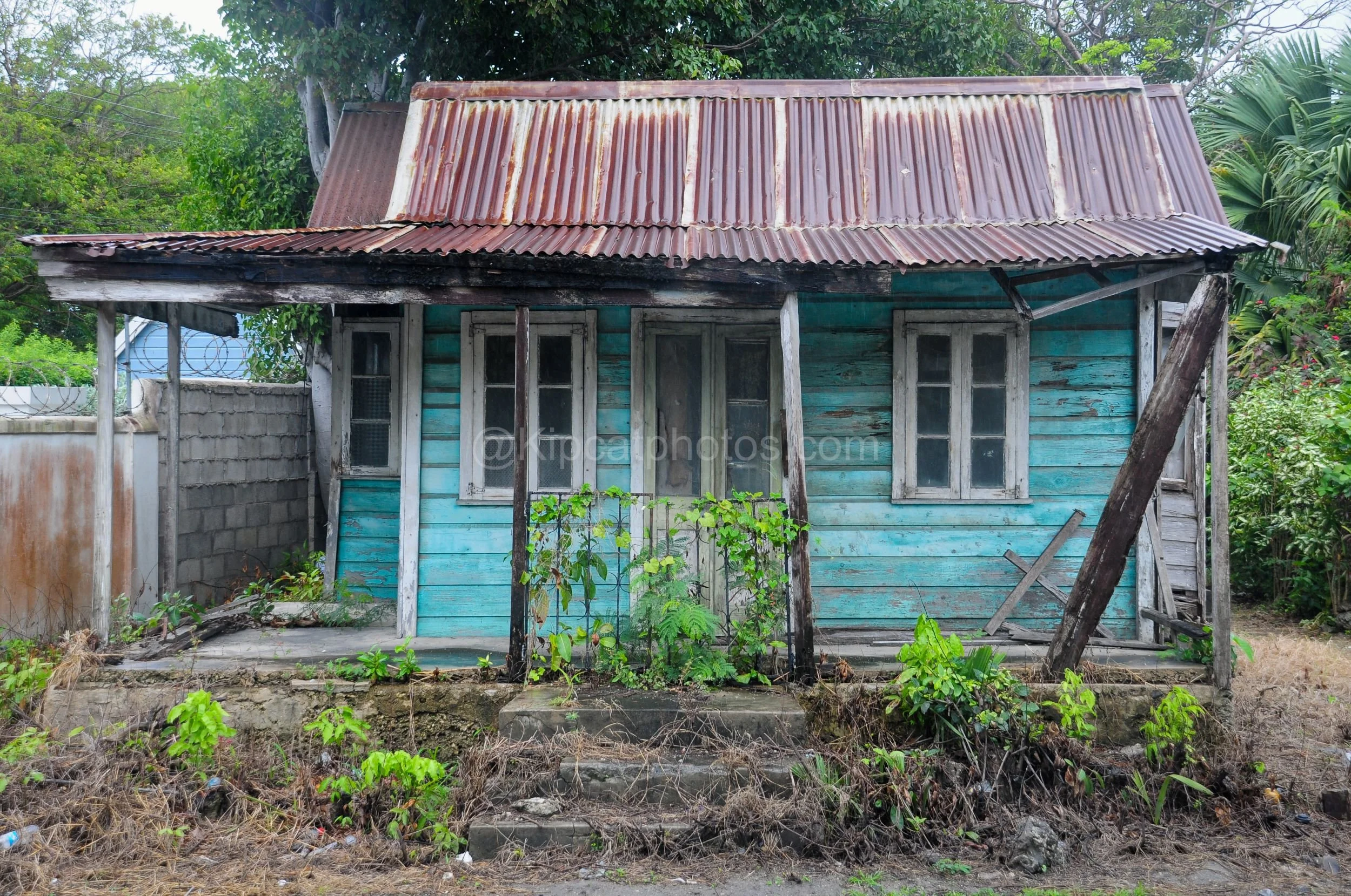 A turquoise chattel house in Barbados with a leaning porch and rusted red roof. Kipcatphotos.com

Faded turquoise boards and a visibly leaning porch post give this chattel house a precarious charm, its window shutters and door frames bleached pale by