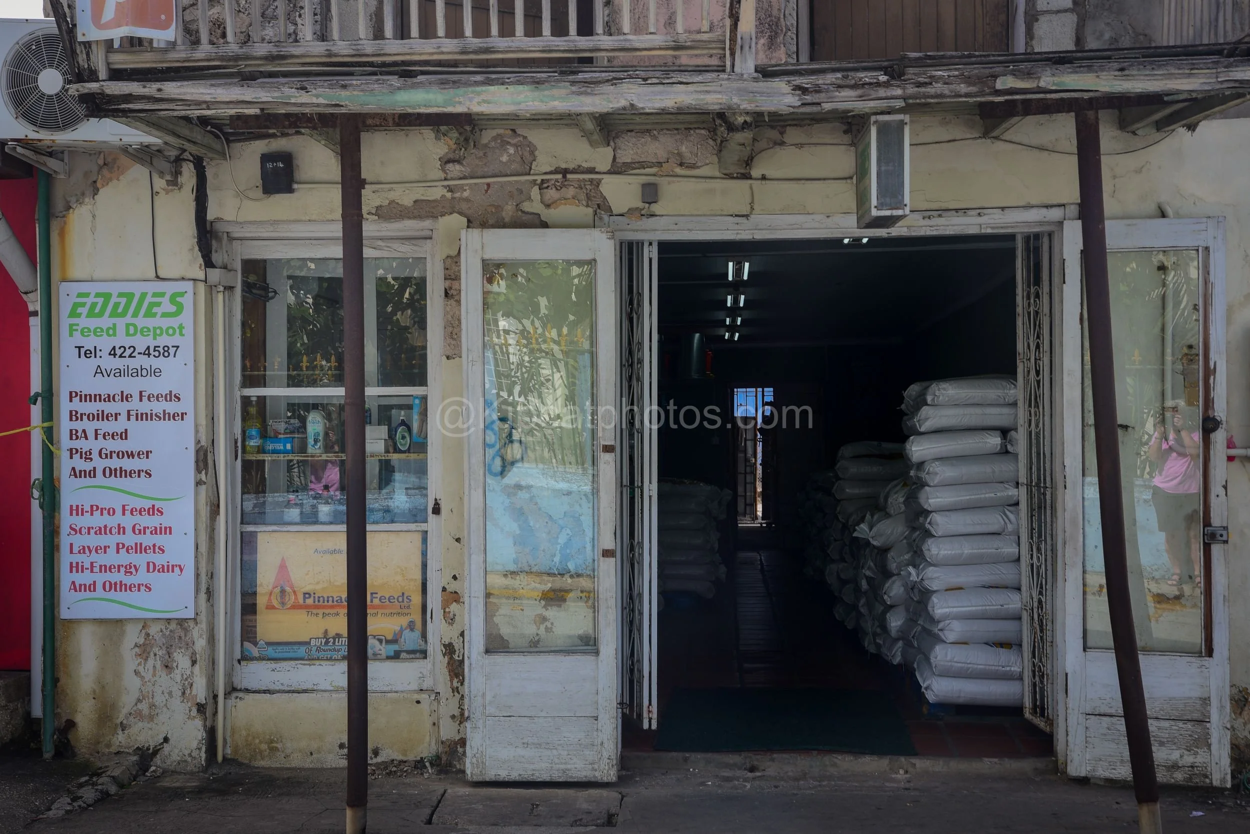A weathered shop front in Speightstown, Barbados, with a hand-painted Eddie's Feed Depot sign and stacked feed bags. Kipcatphotos.com

The peeling plaster and rusted awning posts of this Speightstown shop front frame a hand-painted sign for Eddie's F