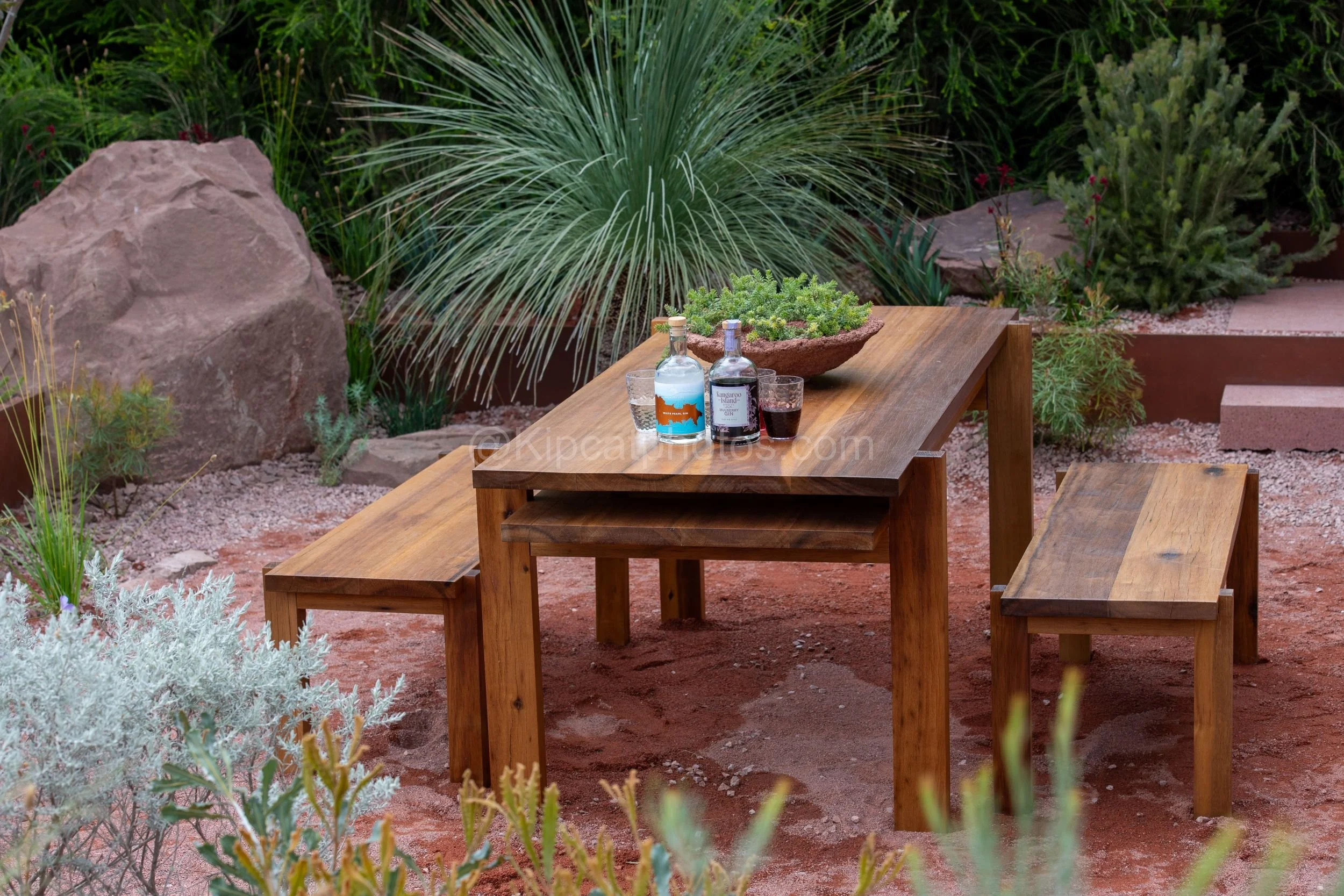 Timber table set with gin bottles and a native planting bowl in the Max Parker-Smith garden at RHS Chelsea Flower Show 2026

A rustic timber table styled with local gin bottles and a stone bowl of succulents, surrounded by grass trees and a large san