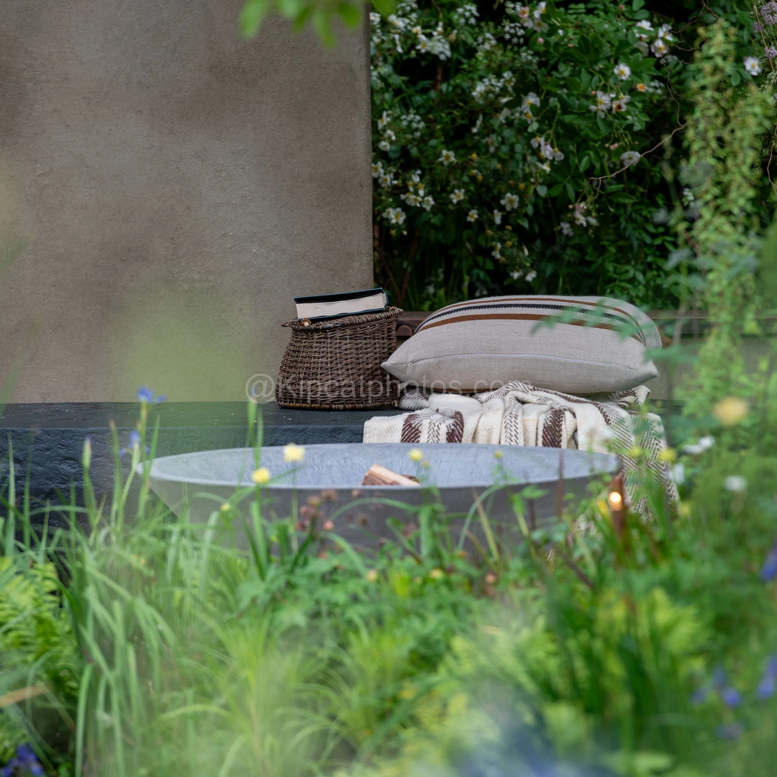 Close-up of cushions, a woven basket and a fire bowl on the seating terrace in the Baz Grainger garden at RHS Chelsea Flower Show 2026

A styled detail shot of a woven basket, book, striped cushions and a stone fire bowl on the terrace seating in the