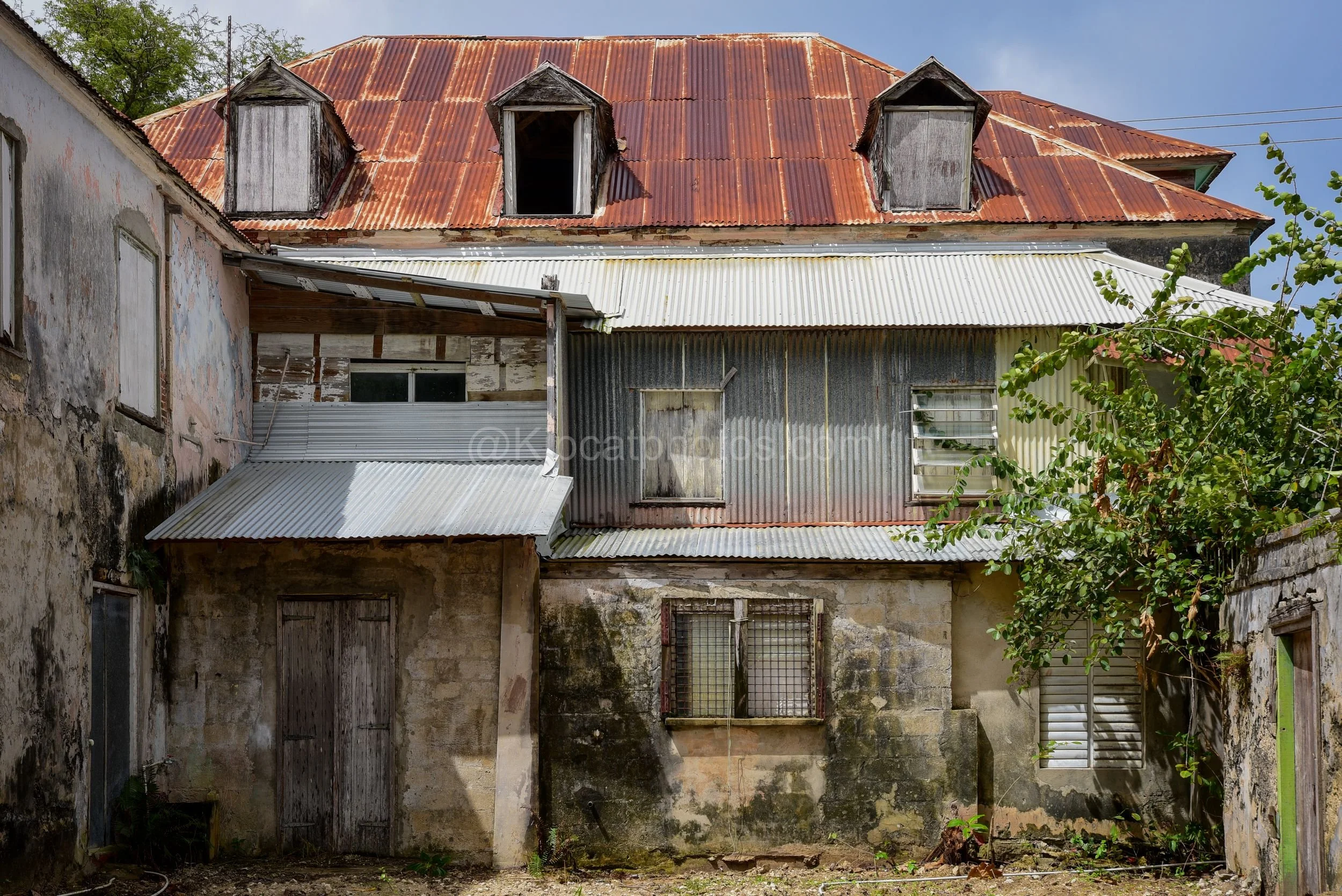 A derelict building in Barbados with a rusted roof, dormer windows and patched corrugated walls. Kipcatphotos.com

Three weathered dormer windows break up this building's rust-streaked roofline, while patched corrugated sheeting and crumbling plaster