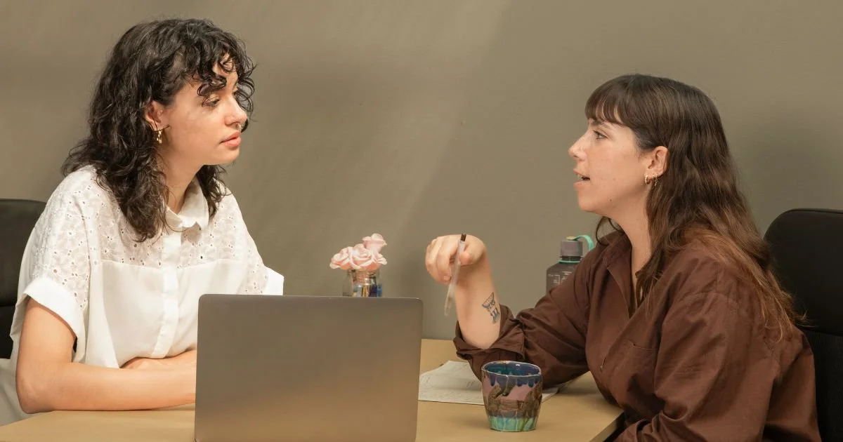 two coworkers talking at a small table with a computer