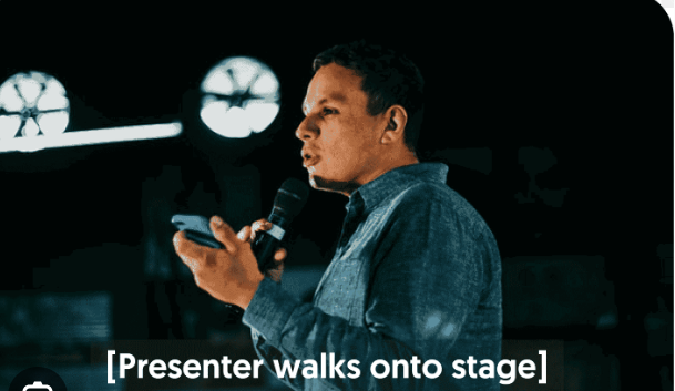 Male speaker in a blue shirt walks onto stage while closed captioning reads "presenter walks onto stage"