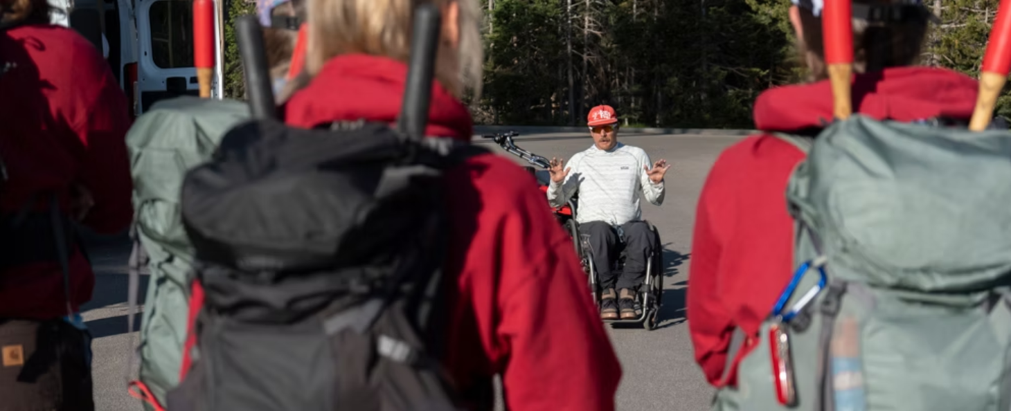 Joe Stone sitting in his wheelchair talking to multiple people with backpacks