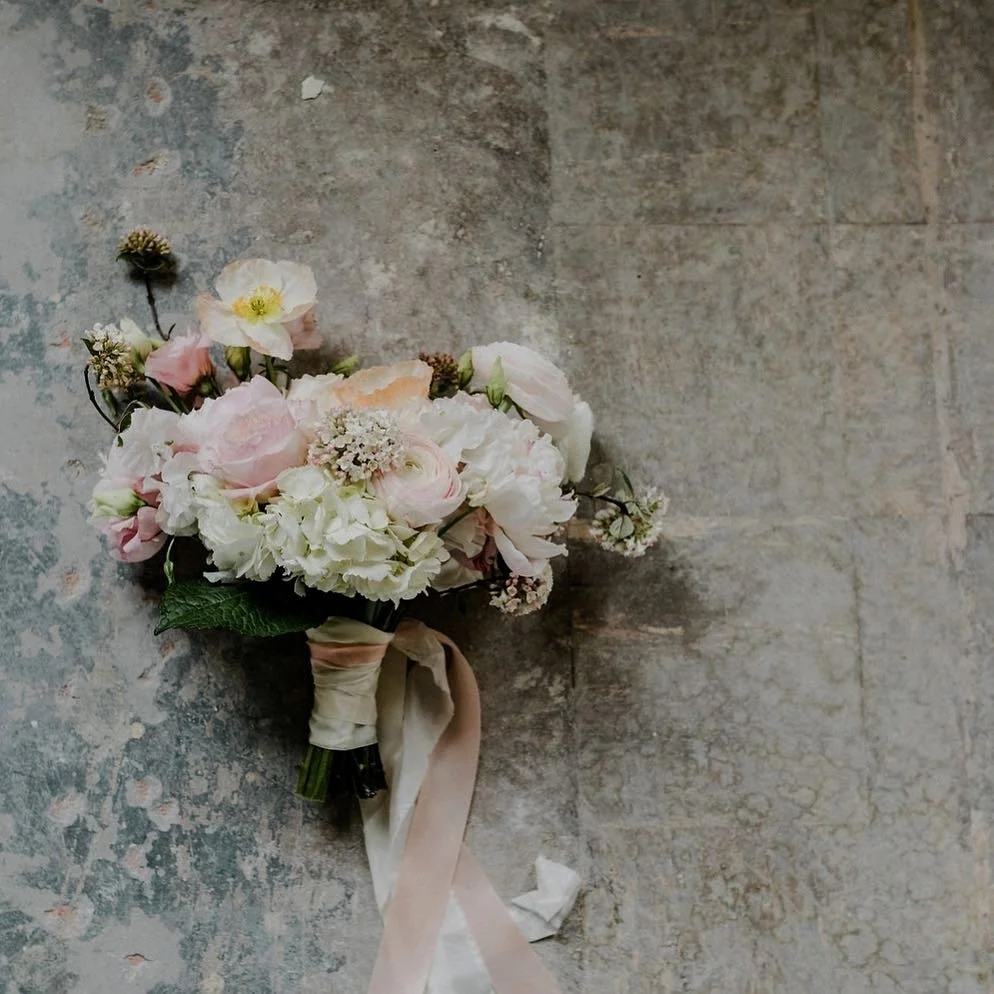 A bouquet of pink and white flowers with green leaves, tied with a beige ribbon on a textured gray surface.