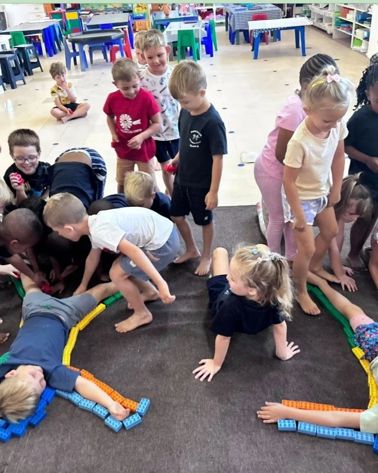 🌈 We Belong Here

First day of school.
New faces. New rooms. Big feelings.

So we start with connection.

Two children lay down.
The class gathers around.
Coloured bricks placed carefully &mdash;
studs up, studs down, orange under arms.

✅Helping ha