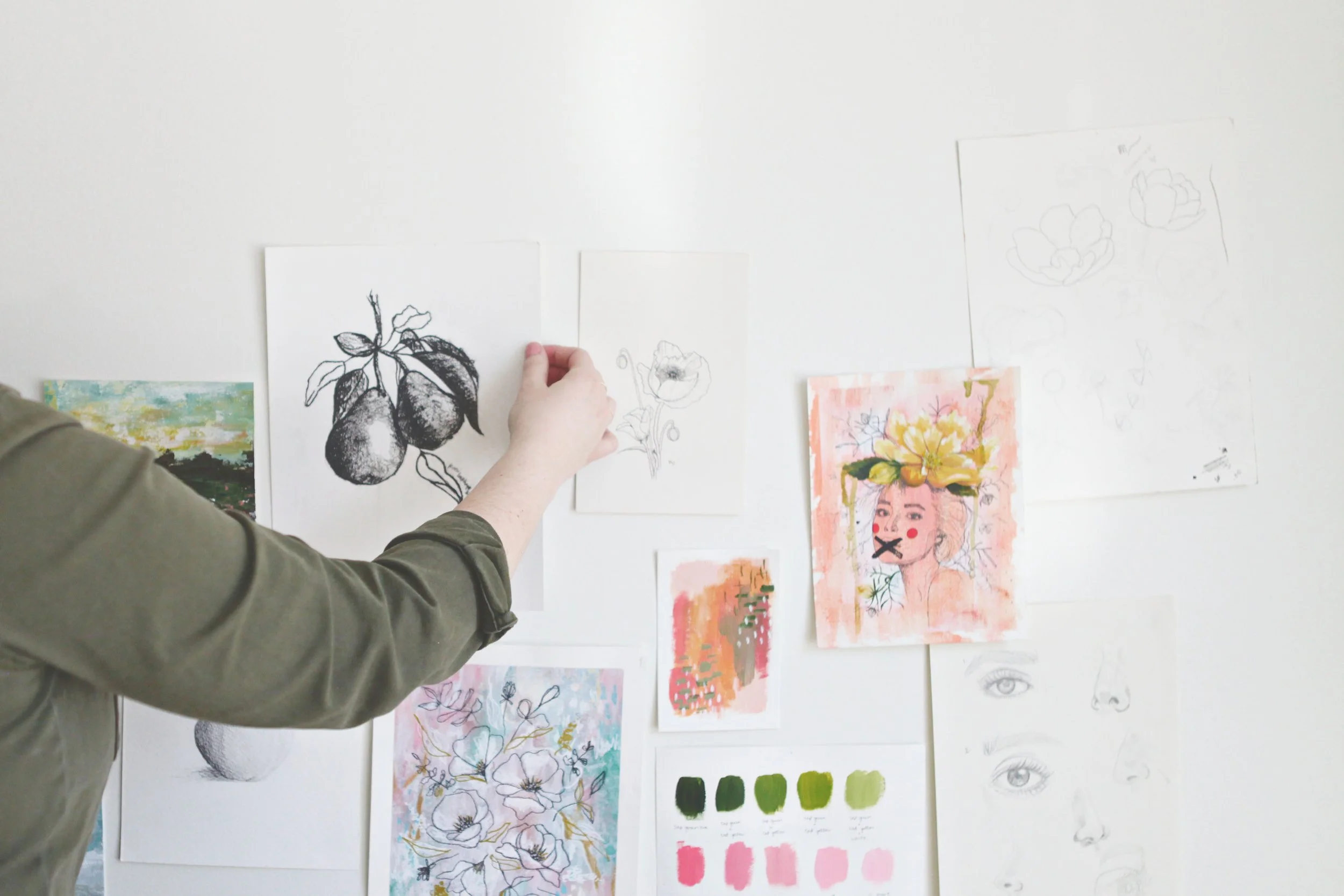 artist's hands hanging pear art on studio wall with floral and landscape art