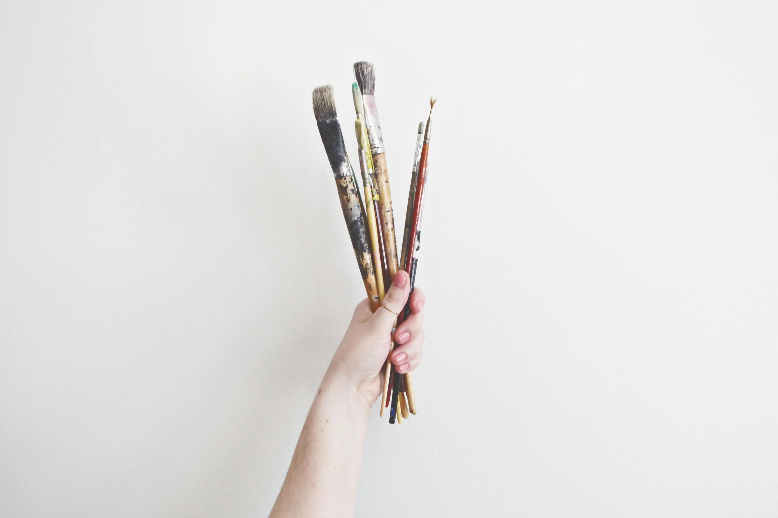artist's hand holding paint brushes covered in paint