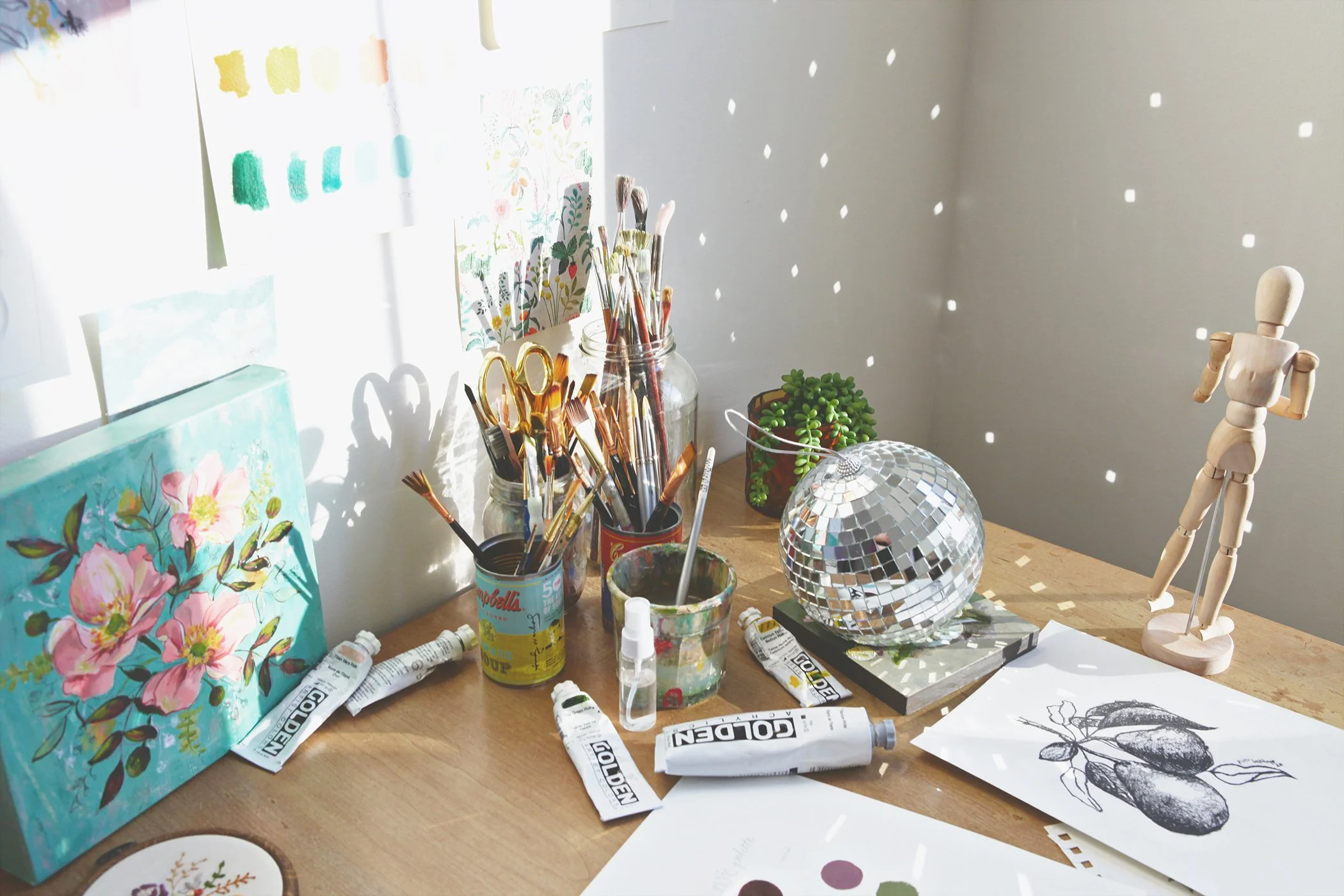 sunlit art studio with paintbrushes, golden paints, and disco ball reflecting light