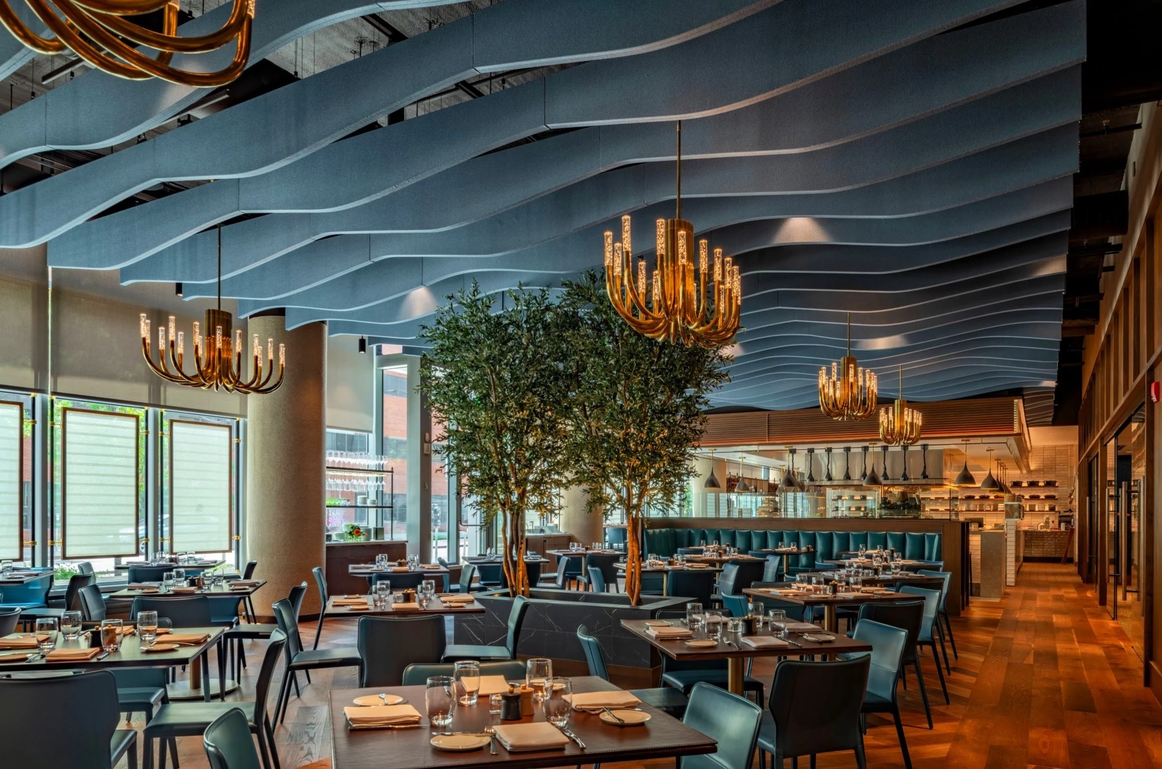 An interior of a restaurant with blue waved ceiling rafters, firework-like chandeliers, and warm, inviting lighting