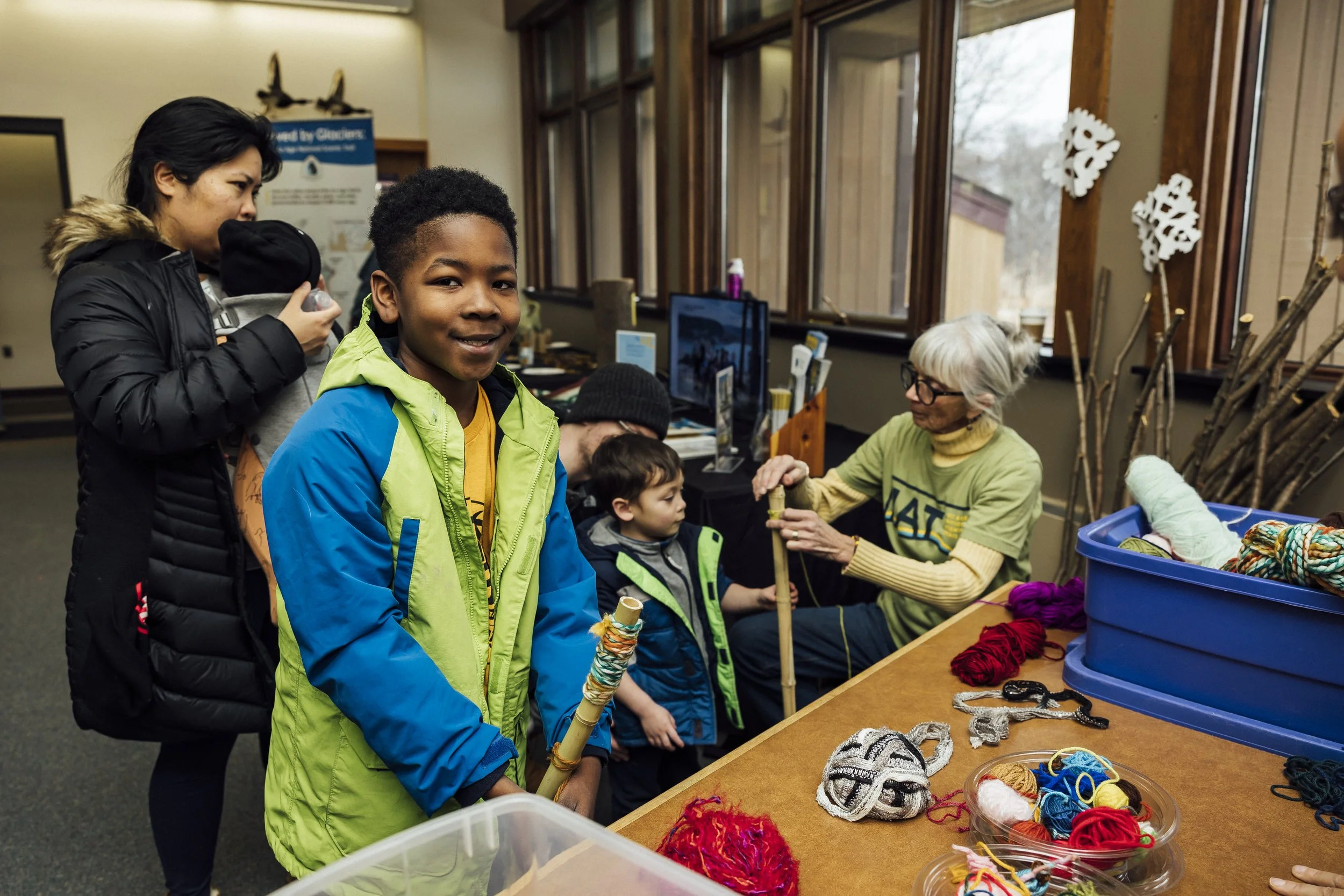 A woman is wrapping a tall hiking stick in yarn.
