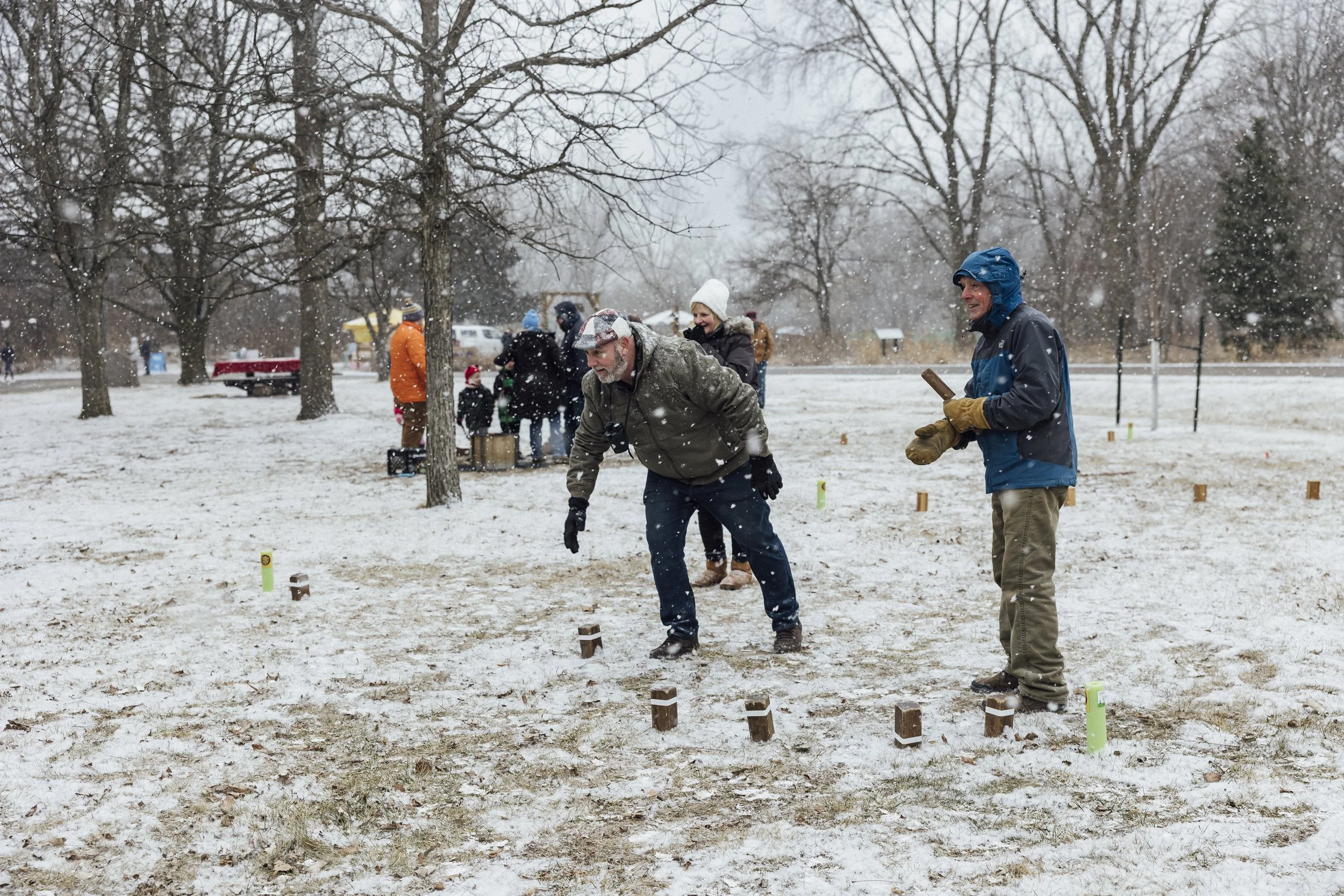 A man tosses wooden sticks in a yard game while snow flurries around him