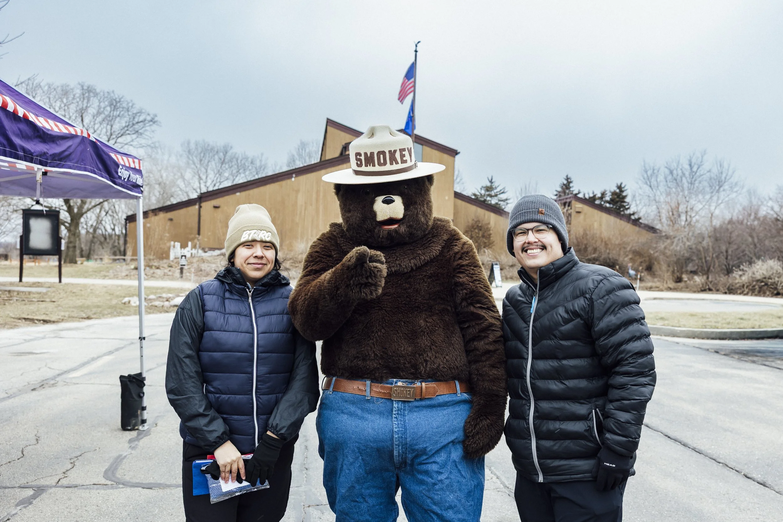 A huge group of outdoor runners are posed in a group photo, with a few of them sporting headbands and hats, and a few in the front doing runners stretches.