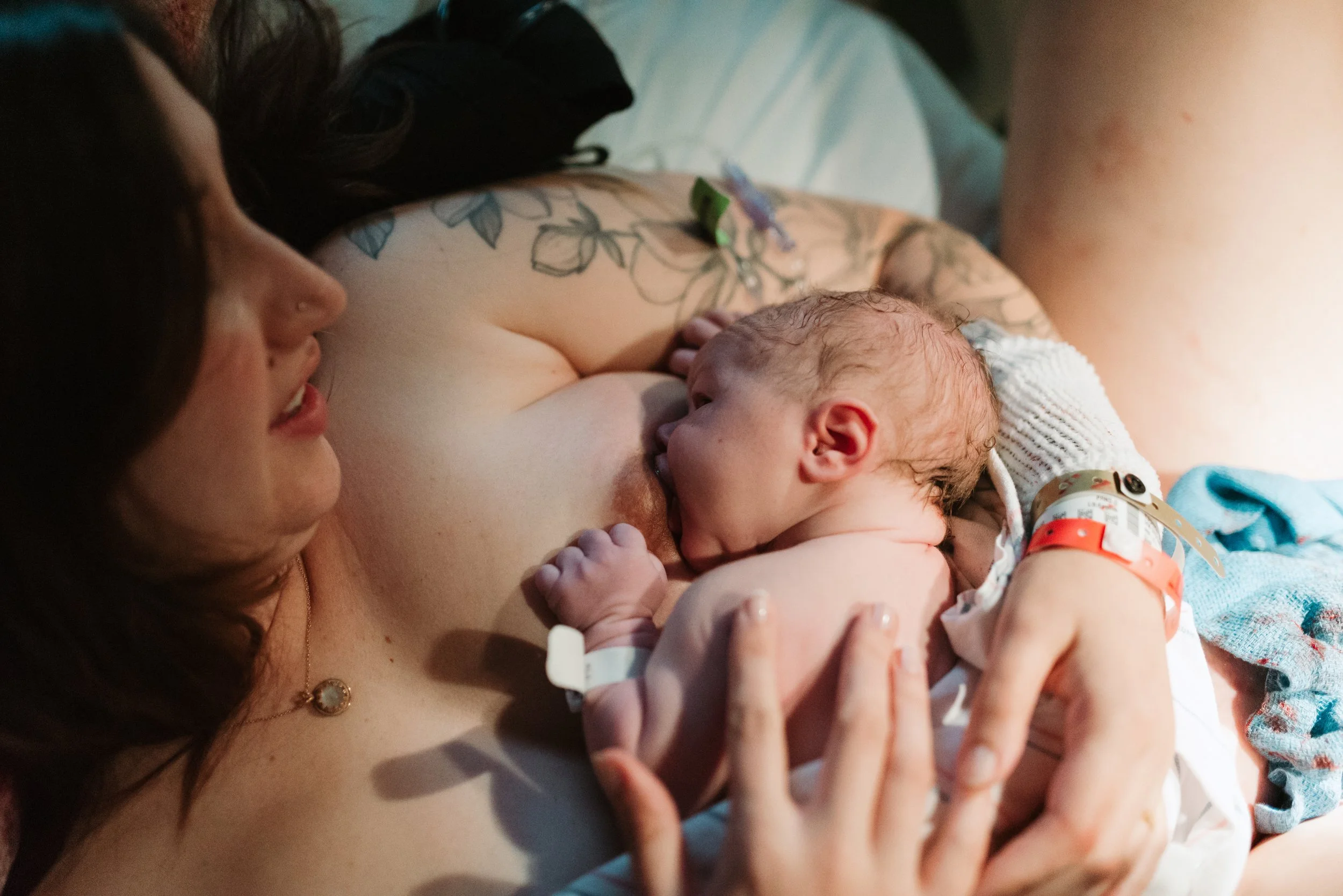 A woman breastfeeding a newborn baby in a hospital bed.