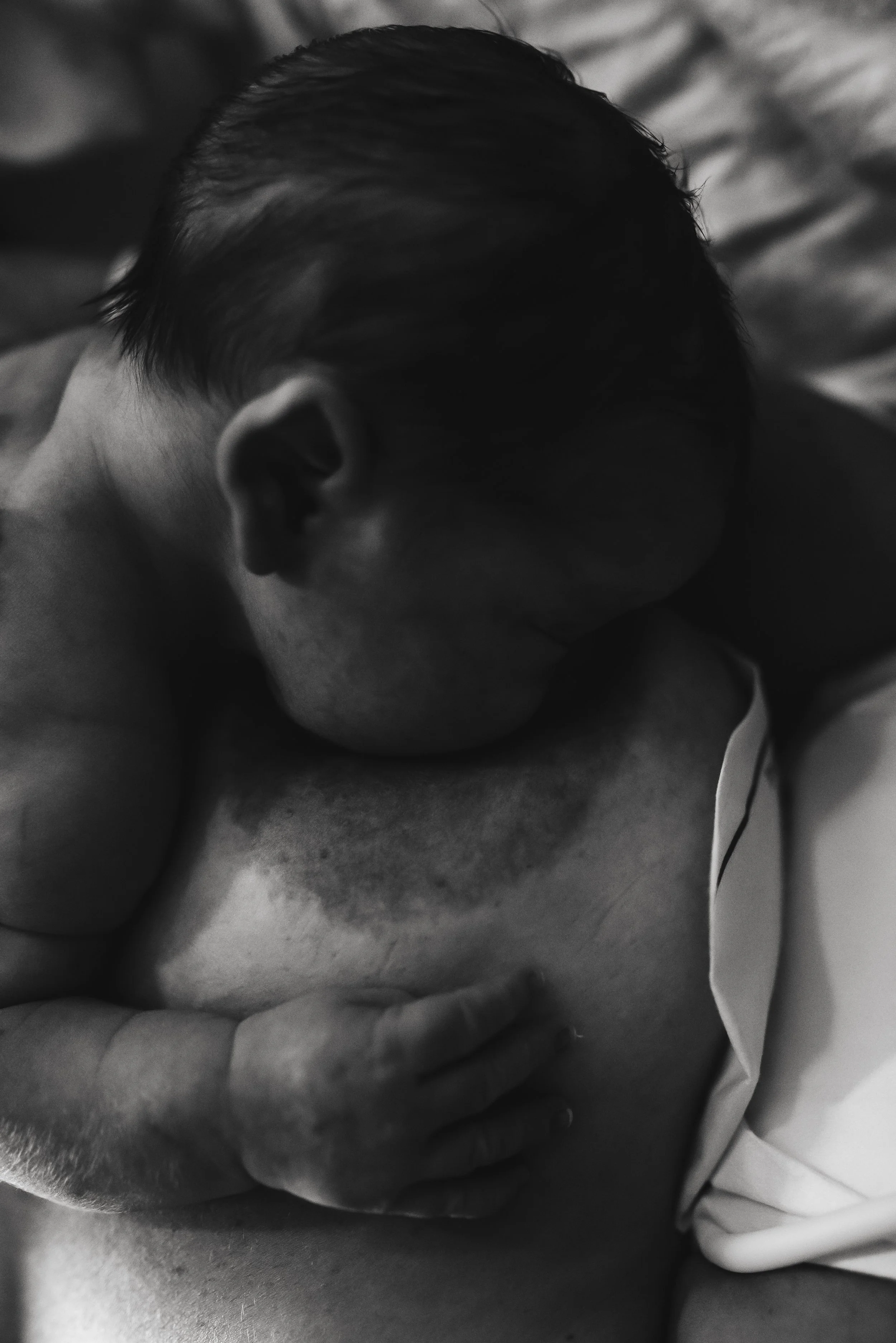 Close-up of a sleeping baby's face with a hand gently touching the cheek, in black and white.