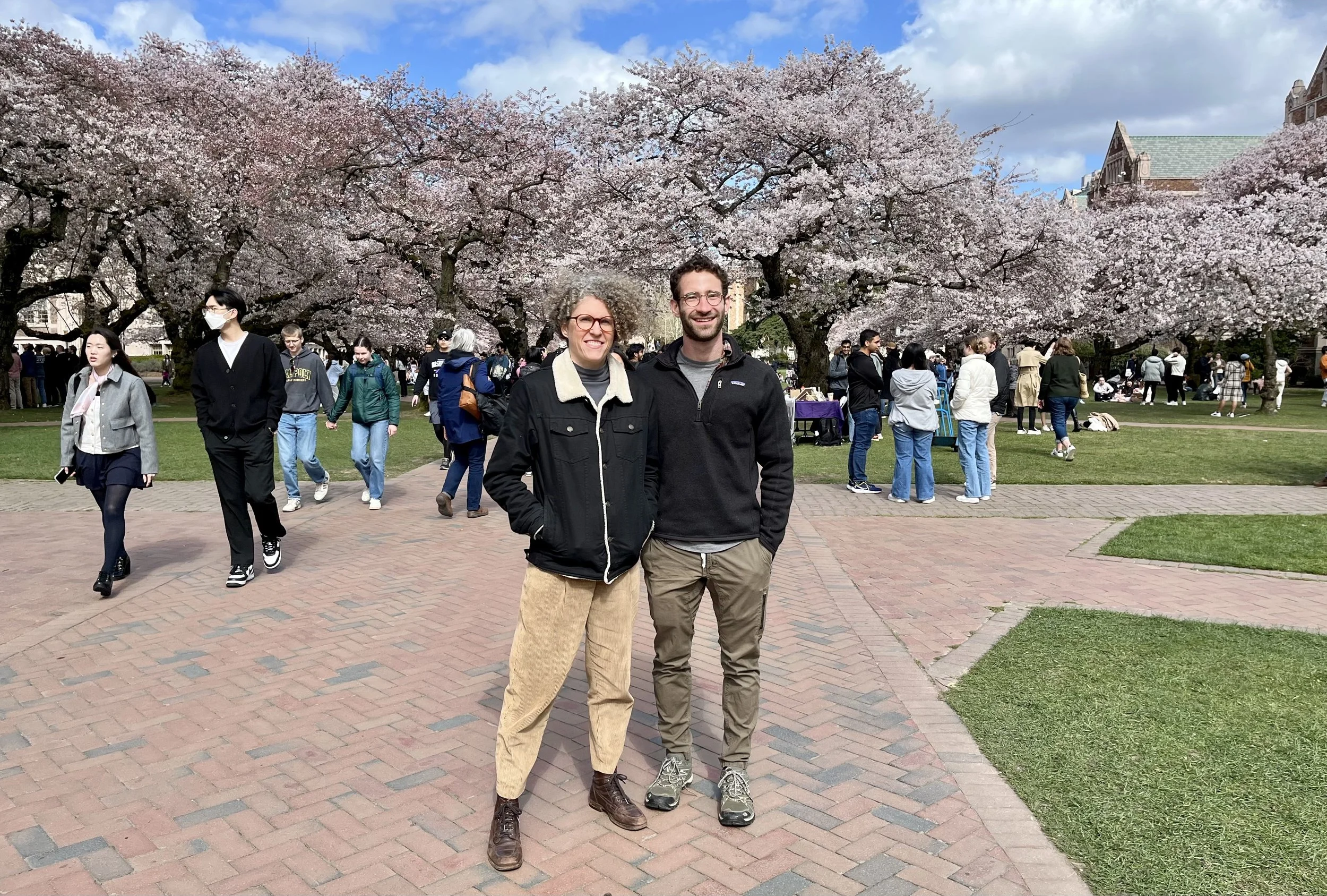 Two people posing for a professional photo near cherry blossoms on the University of Washington campus.