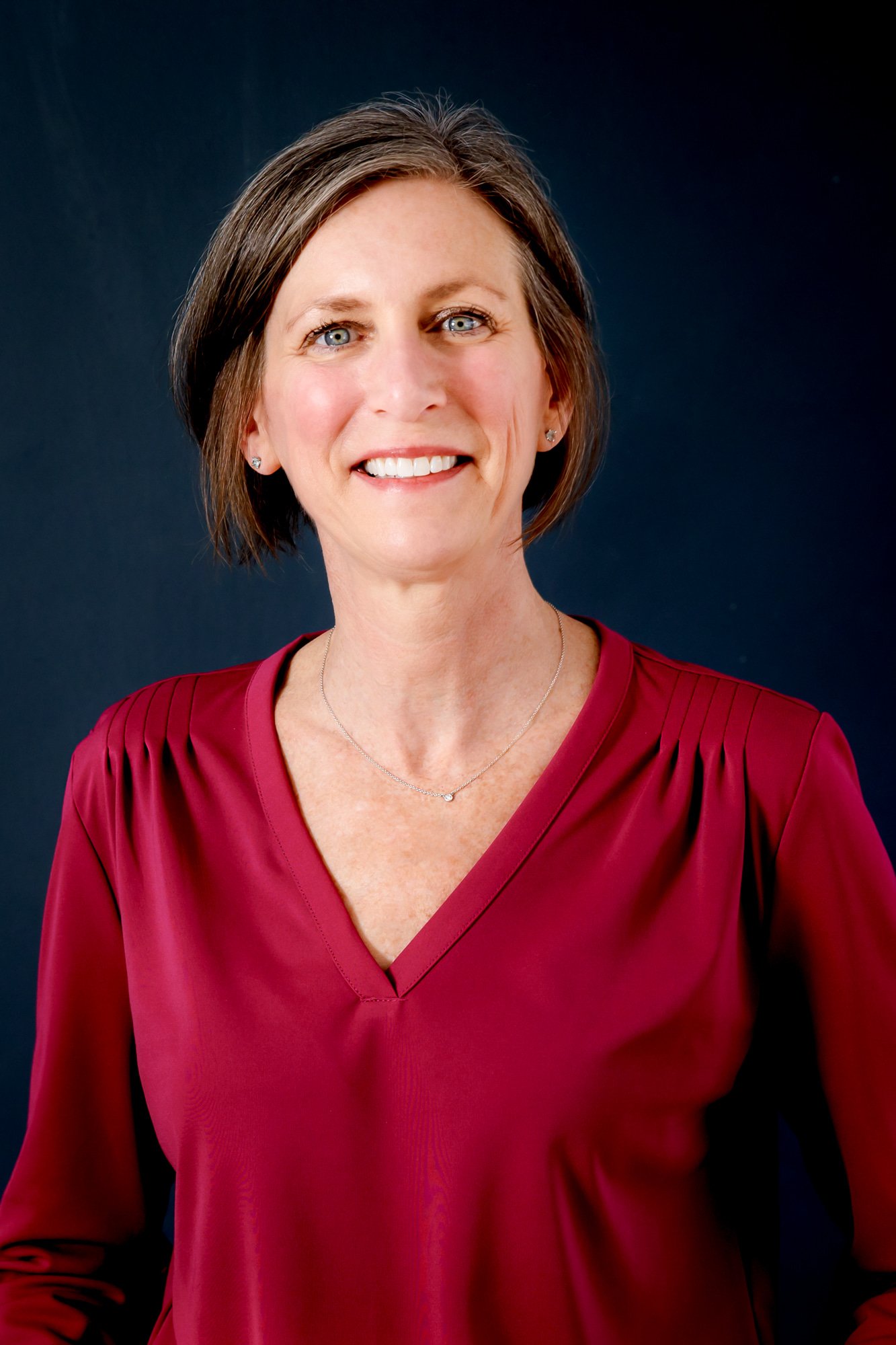 Smiling woman in a red blouse against a dark background.
