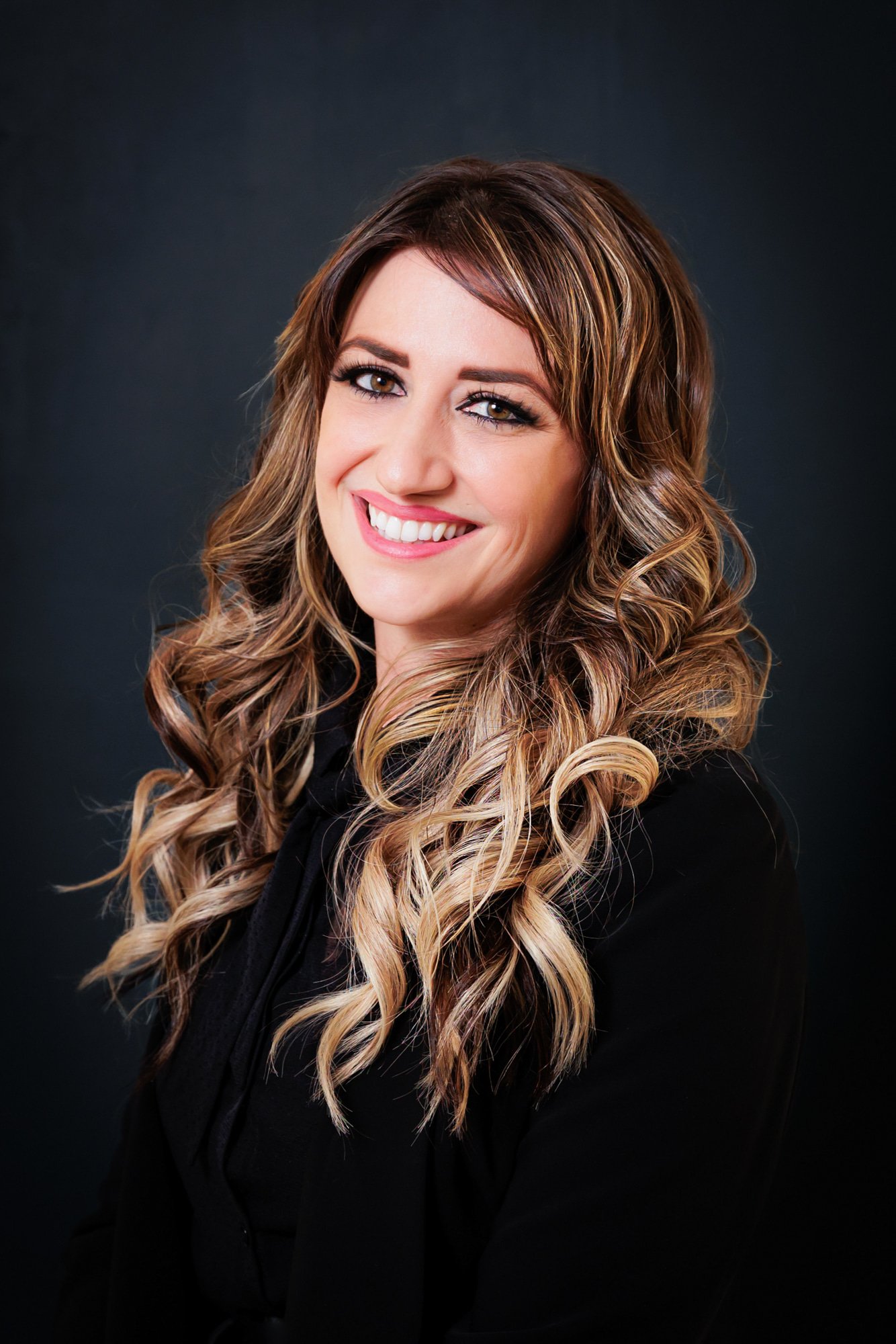 Woman with long wavy hair and a black top smiling against a dark background