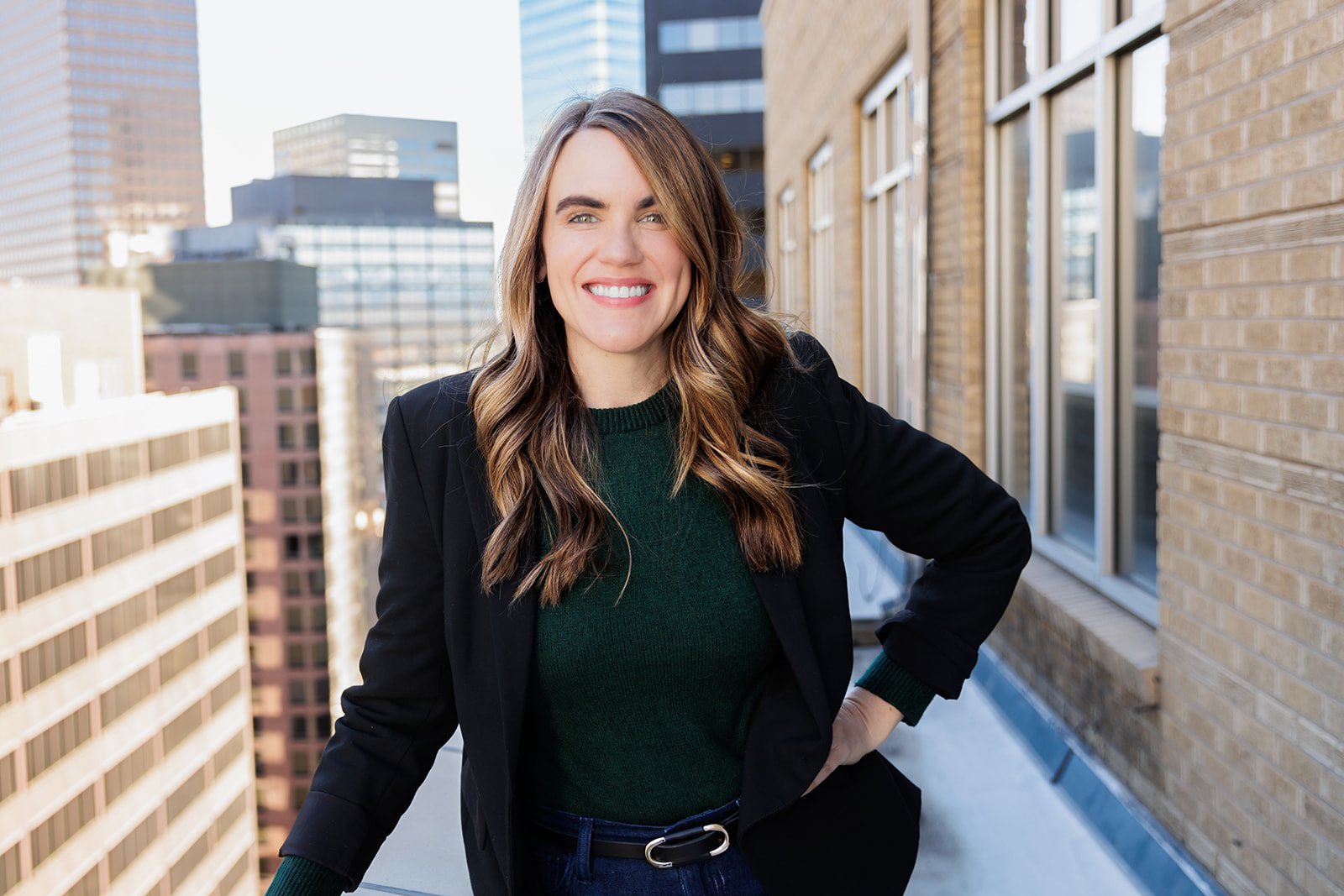 Smiling woman standing on an urban rooftop with city buildings in the background.