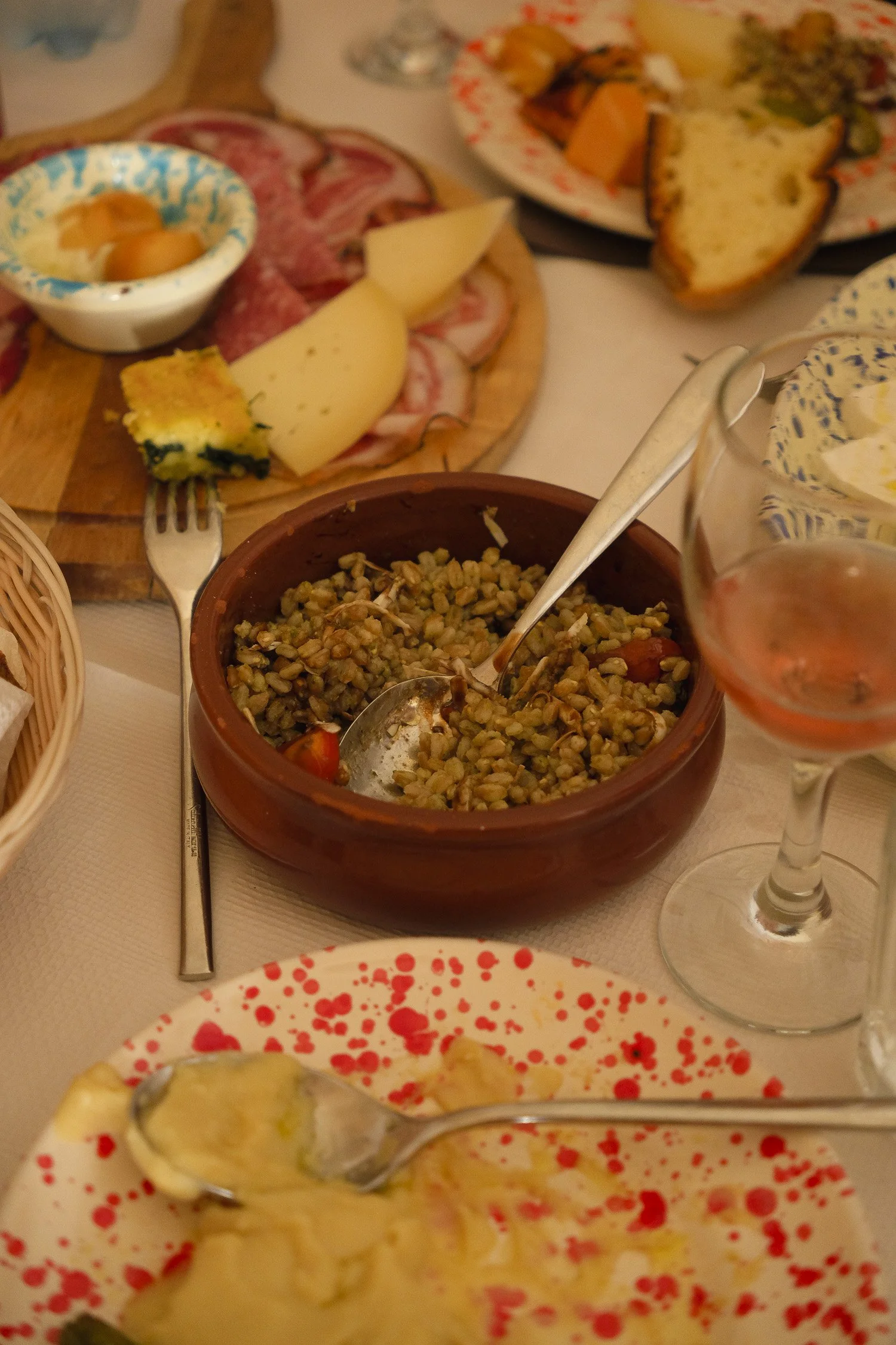 A shared lunch in Grottaglie, Italy with mismatched crockery, simple local dishes, and wine glasses on a crowded table.