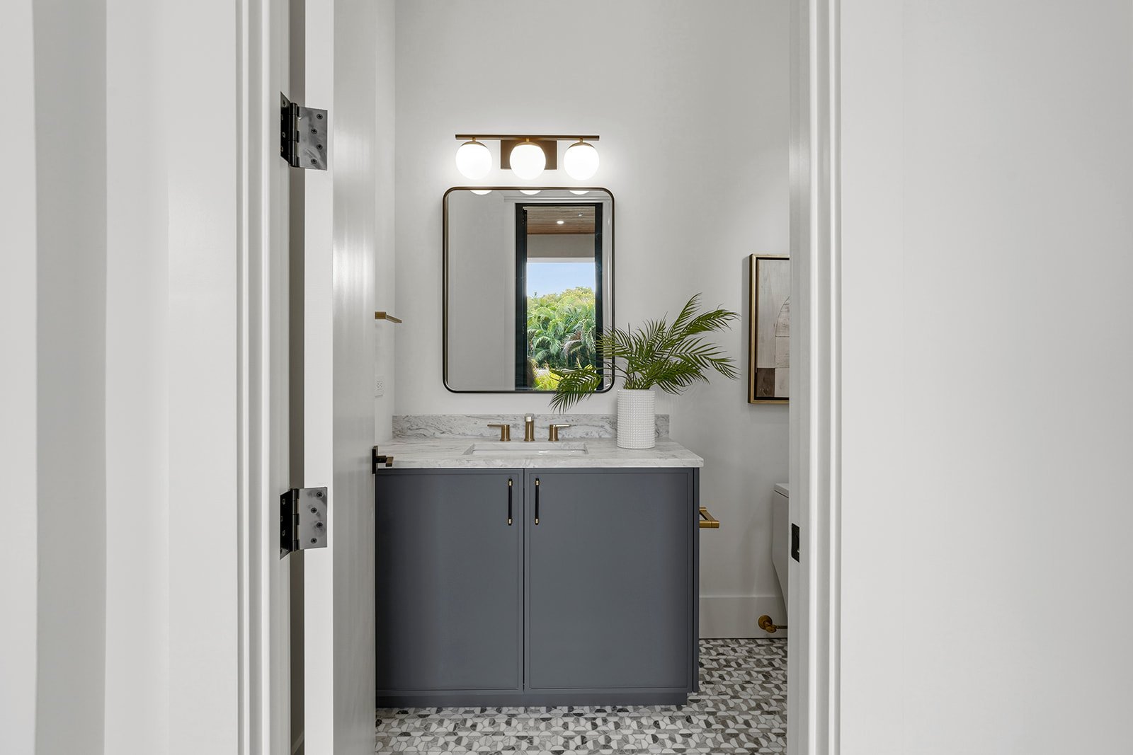 Modern bathroom with a single vanity, gray cabinet, white marble countertop, oval mirror, potted plant, and three globe lights.