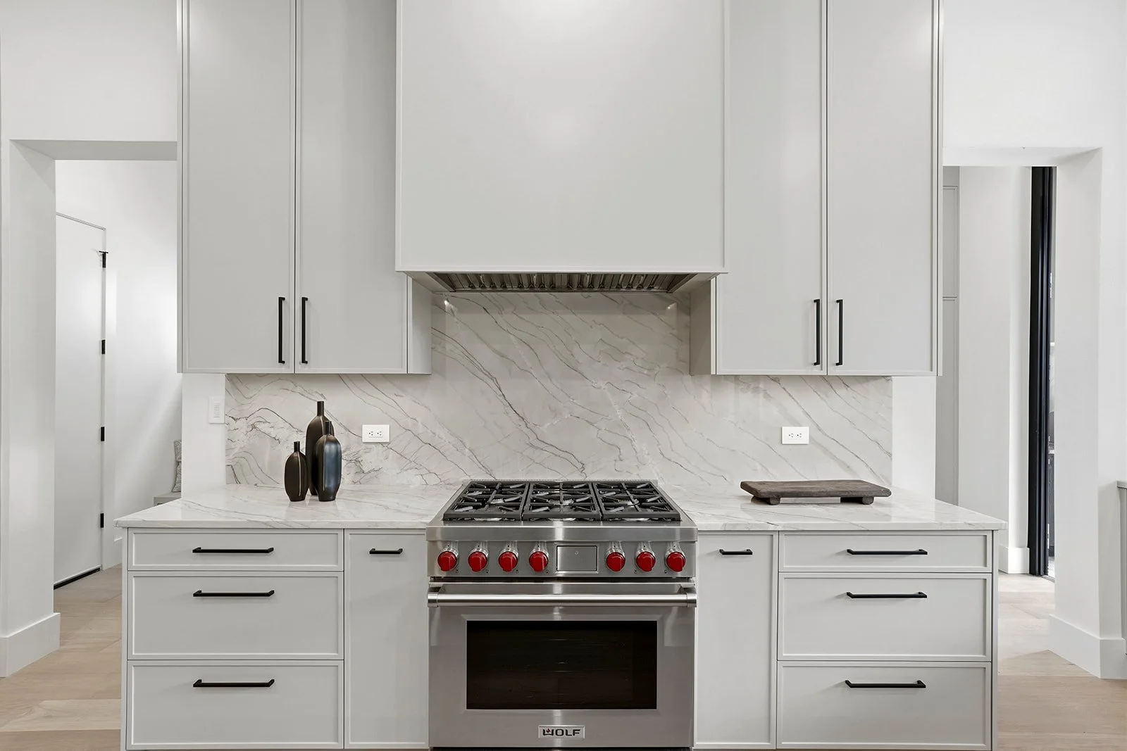 Modern kitchen with white cabinets, marble backsplash, and a stainless steel stove with red knobs.