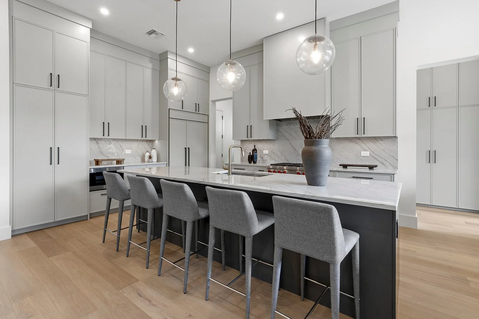 Modern kitchen with white cabinets, marble backsplash, island with seating, grey stools, and pendant lighting.