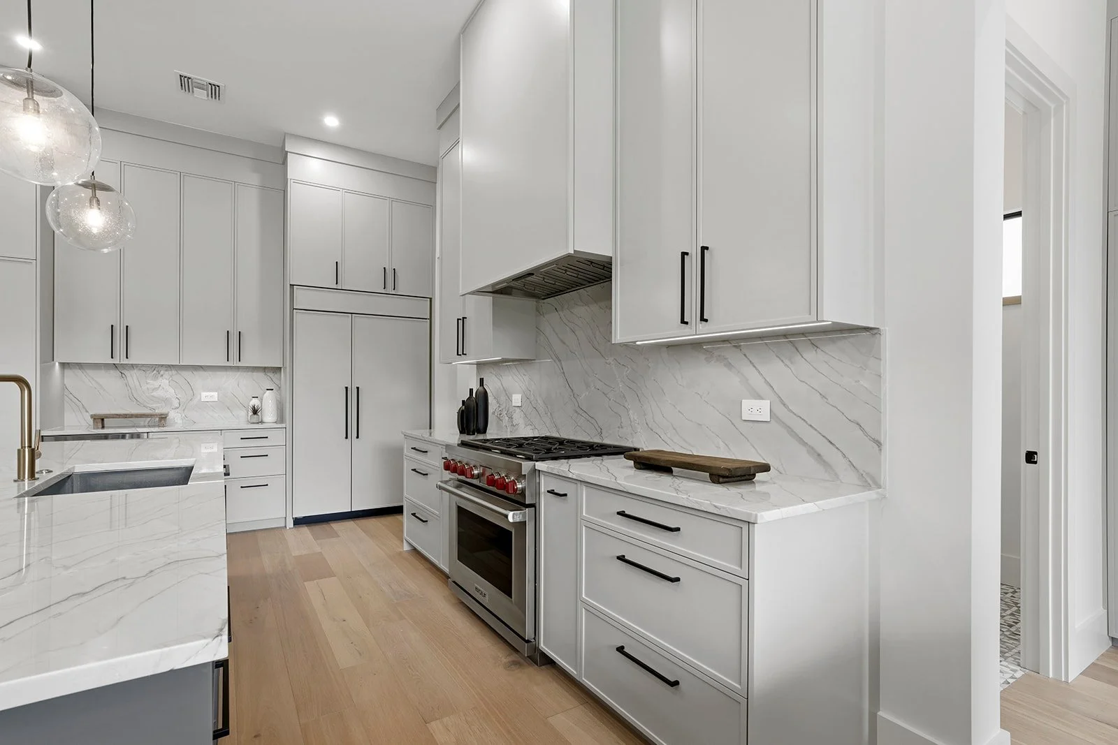 Modern kitchen with white cabinetry, marble countertops, a stainless steel stove with red knobs, and wooden flooring.
