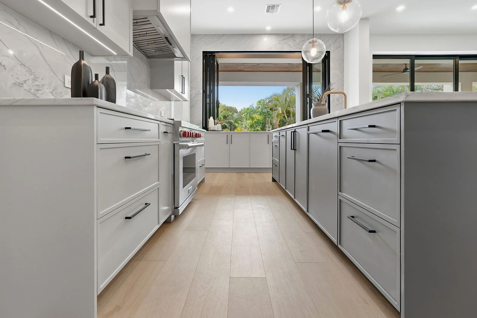 Modern kitchen with white and gray cabinetry, a stainless steel stove, and a large window with a scenic view of greenery.