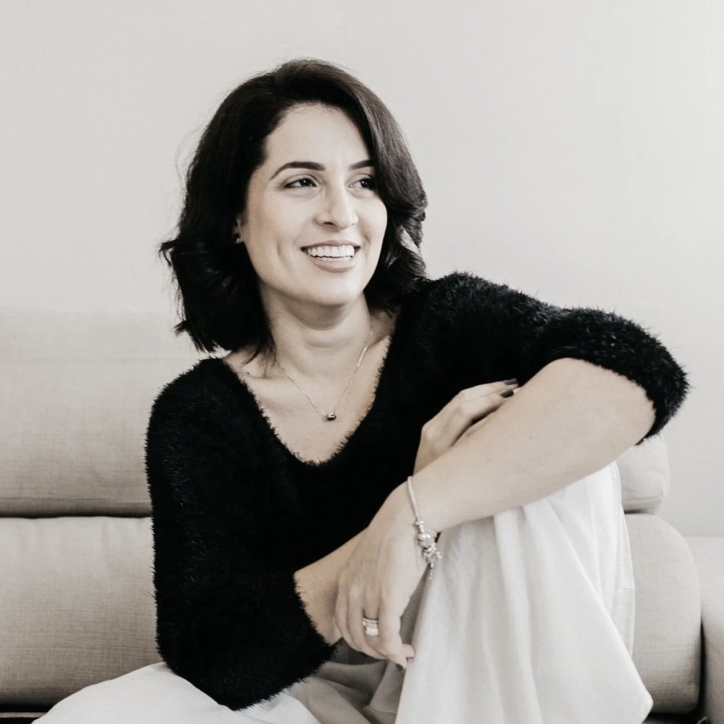 An image of author Gina Solatura, a woman with dark brown, shoulder-length hair smiling and sitting on a beige sofa.