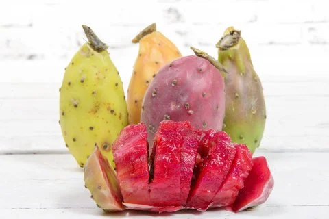A variety of prickly pear fruits, including sliced and whole pieces, on a white table top.