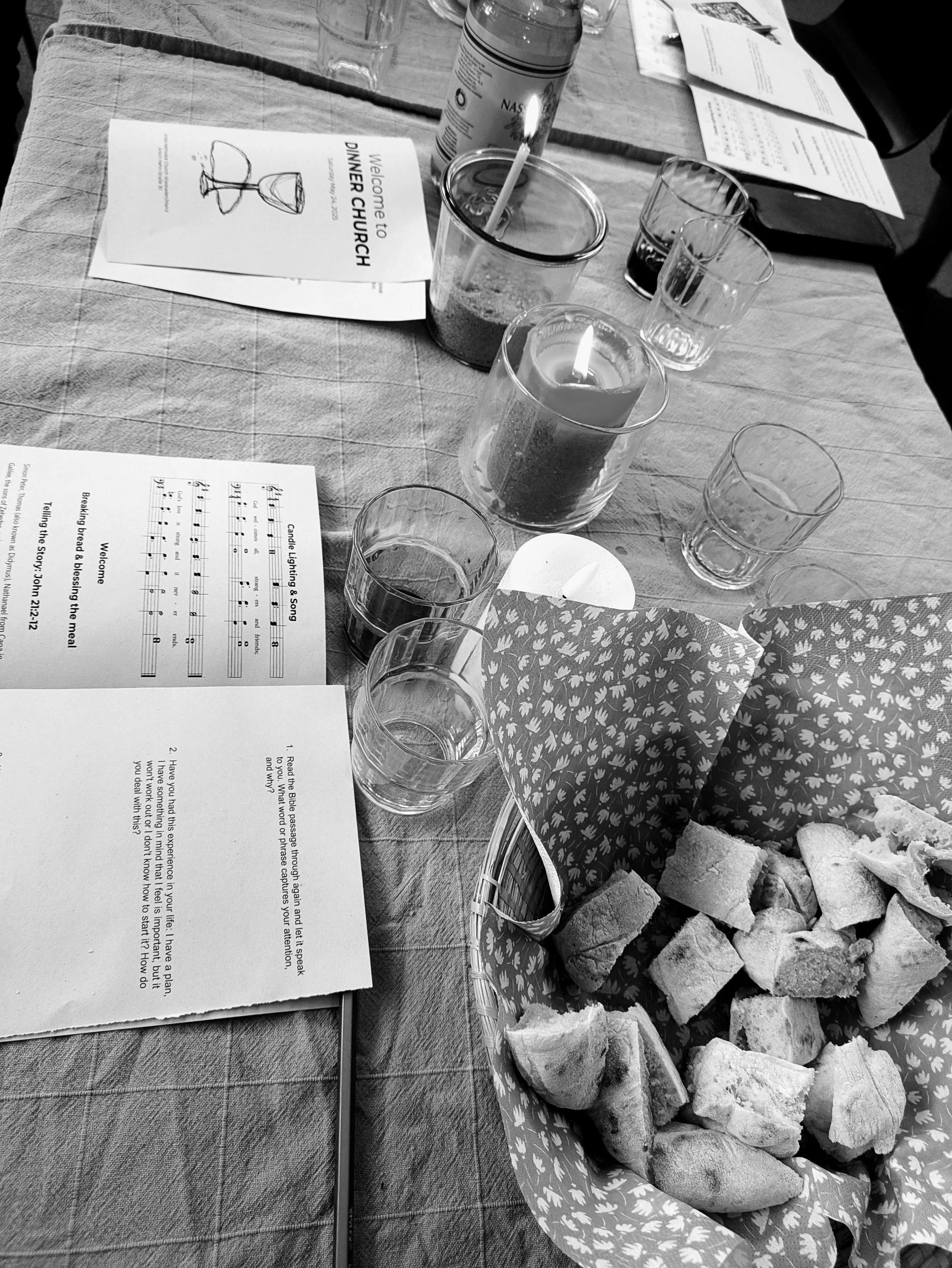 A table set for a church event with bread, candles, glasses of water, and hymn sheets, including a song titled 'Candle Lighting & Song' and sheet music.