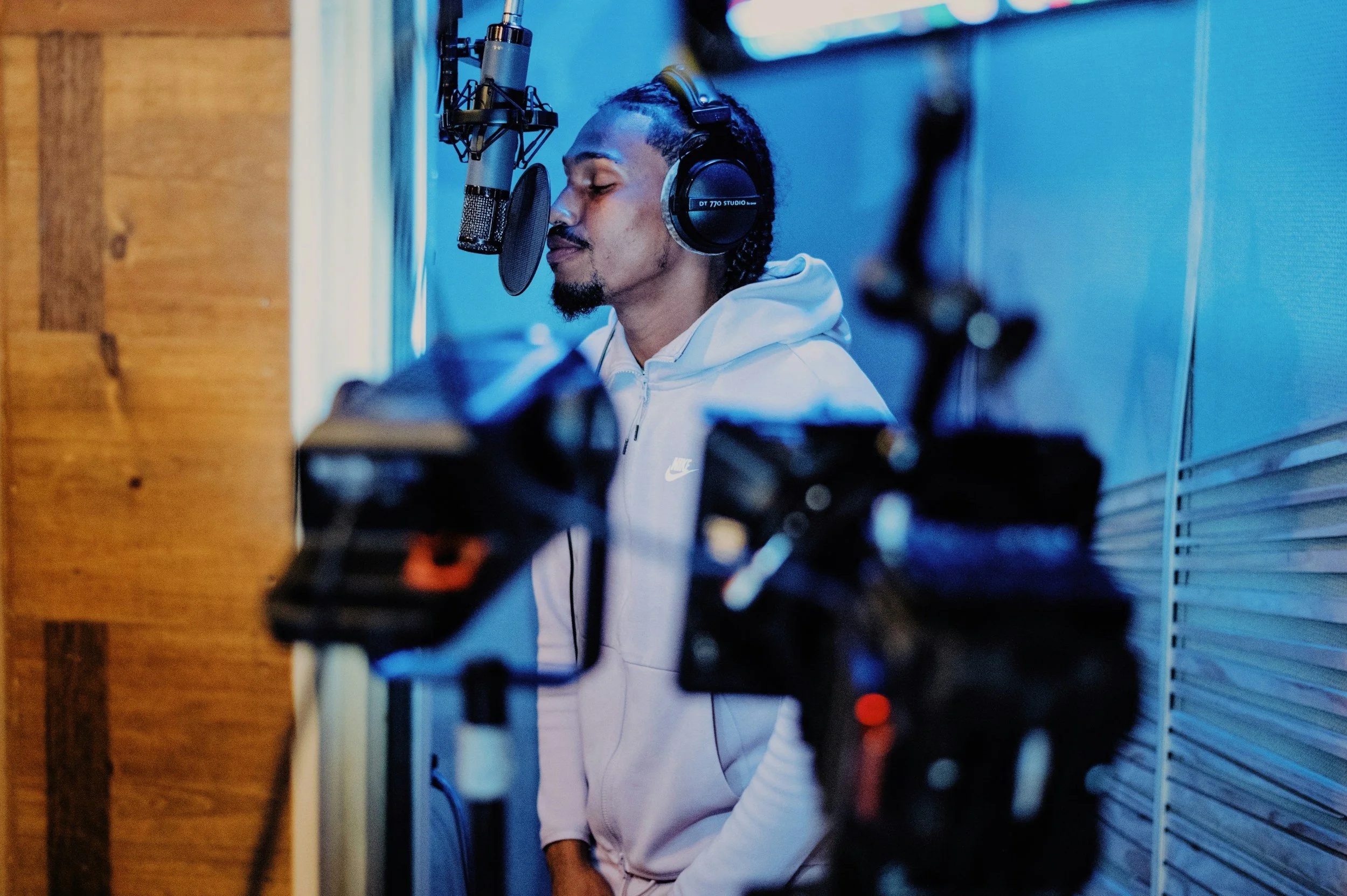 Ein Mann im Aufnahmestudio trägt Kopfhörer und singt vor einem Mikrofon, während er im Tonstudio arbeitet.