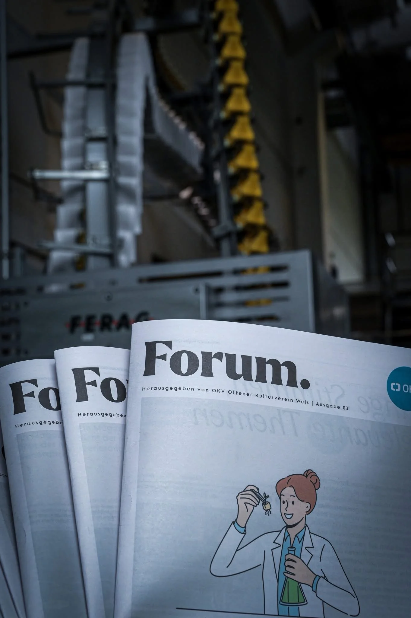 Mehrere rote und weiße Magazine mit der Überschrift 'Forum', einer Zeichnung eines Wissenschaftlers in einem weißen Laborkittel, der ein Reagenzglas hält und lächelt, im Vordergrund, im Hintergrund eine industrielle Einrichtung.