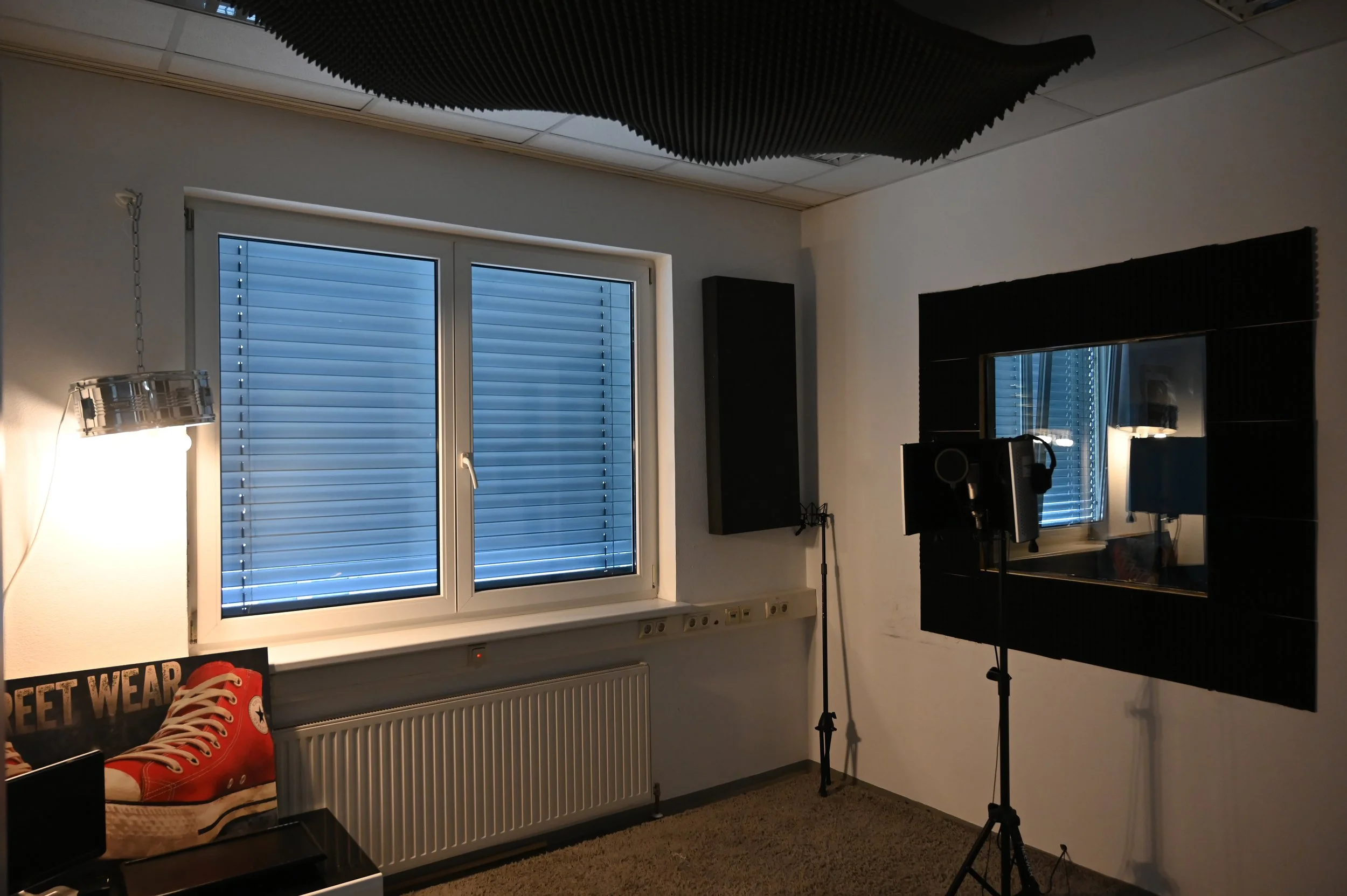 Ein Zimmer mit einem Fenster, Musikanlage, Mikrofonständer und Akustikschaumstoff an der Wand.
