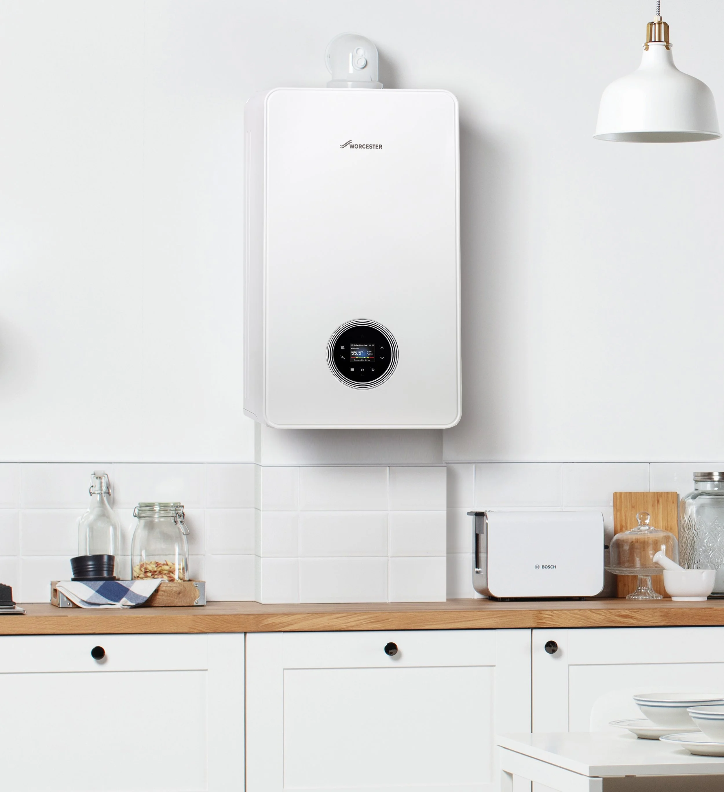 White wall-mounted Worcester boiler in a modern kitchen with a wooden countertop, glass bottles, a Bosch toaster, glass jars, a cutting board, and dishes.