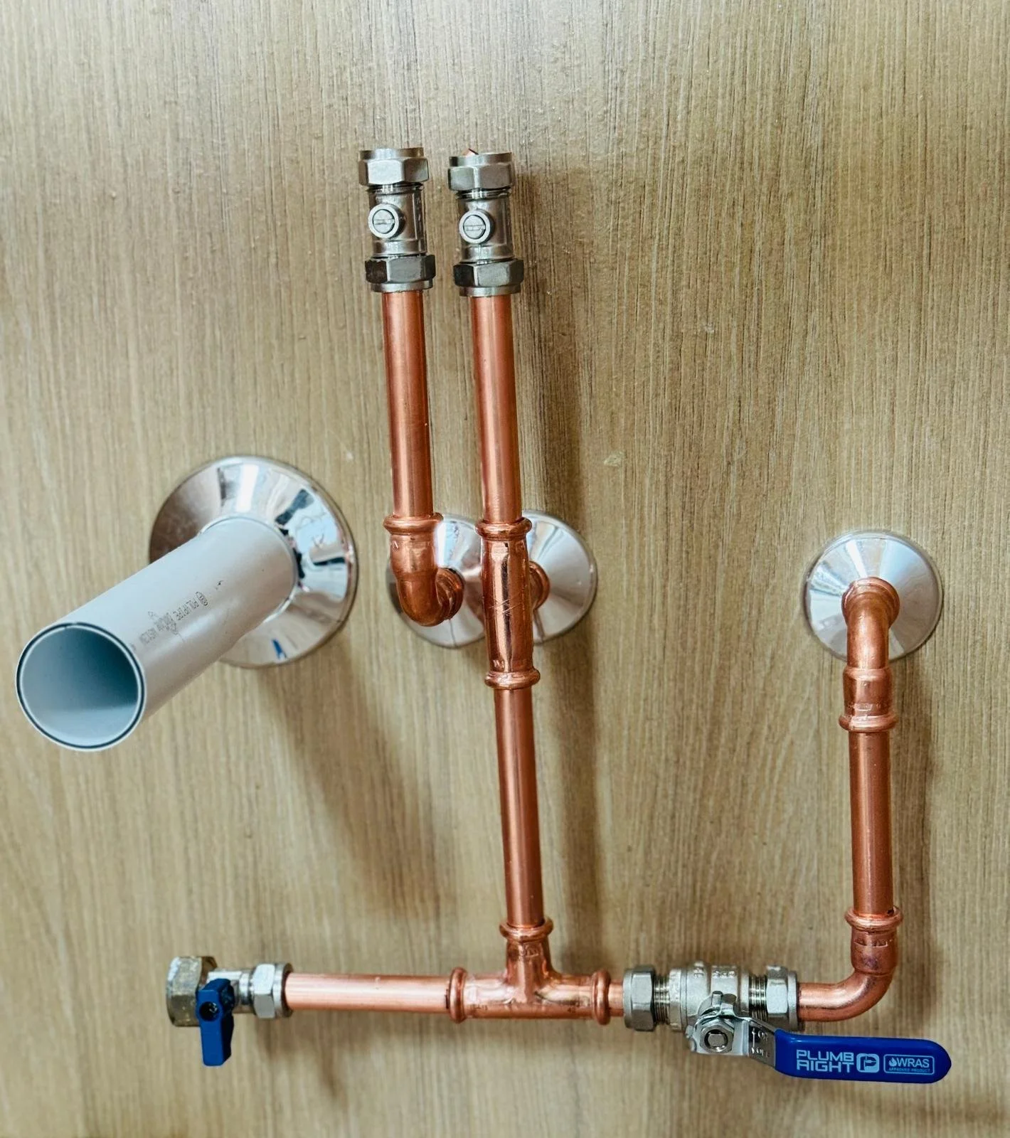Copper plumbing pipes with shut-off valves mounted on a wooden wall.
