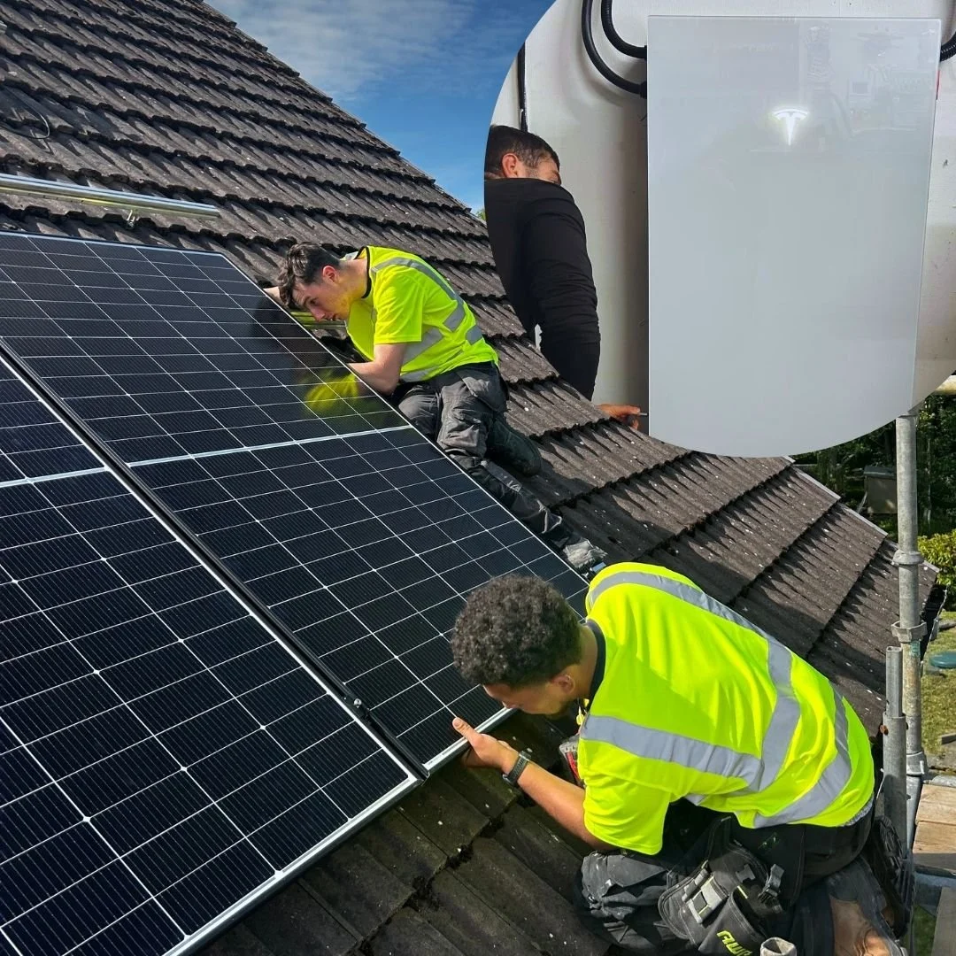 Three workers in yellow safety vests installing or repairing solar panels on a sloped roof, with a large white satellite dish or antenna nearby.